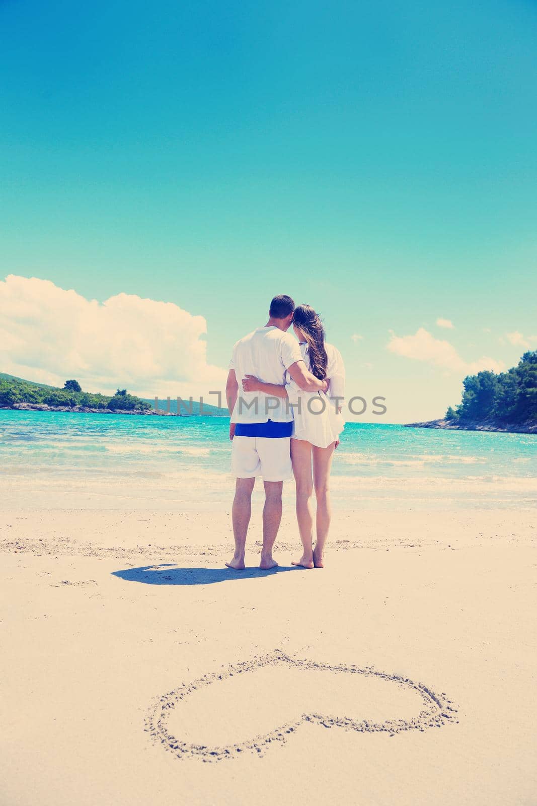 happy young couple have fun and relax  on the summer with heart drawing on beach sand