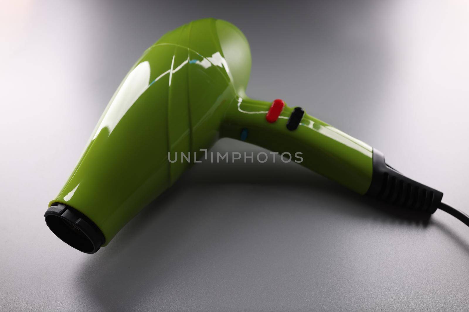 Green professional hair dryer lying on gray background closeup by kuprevich