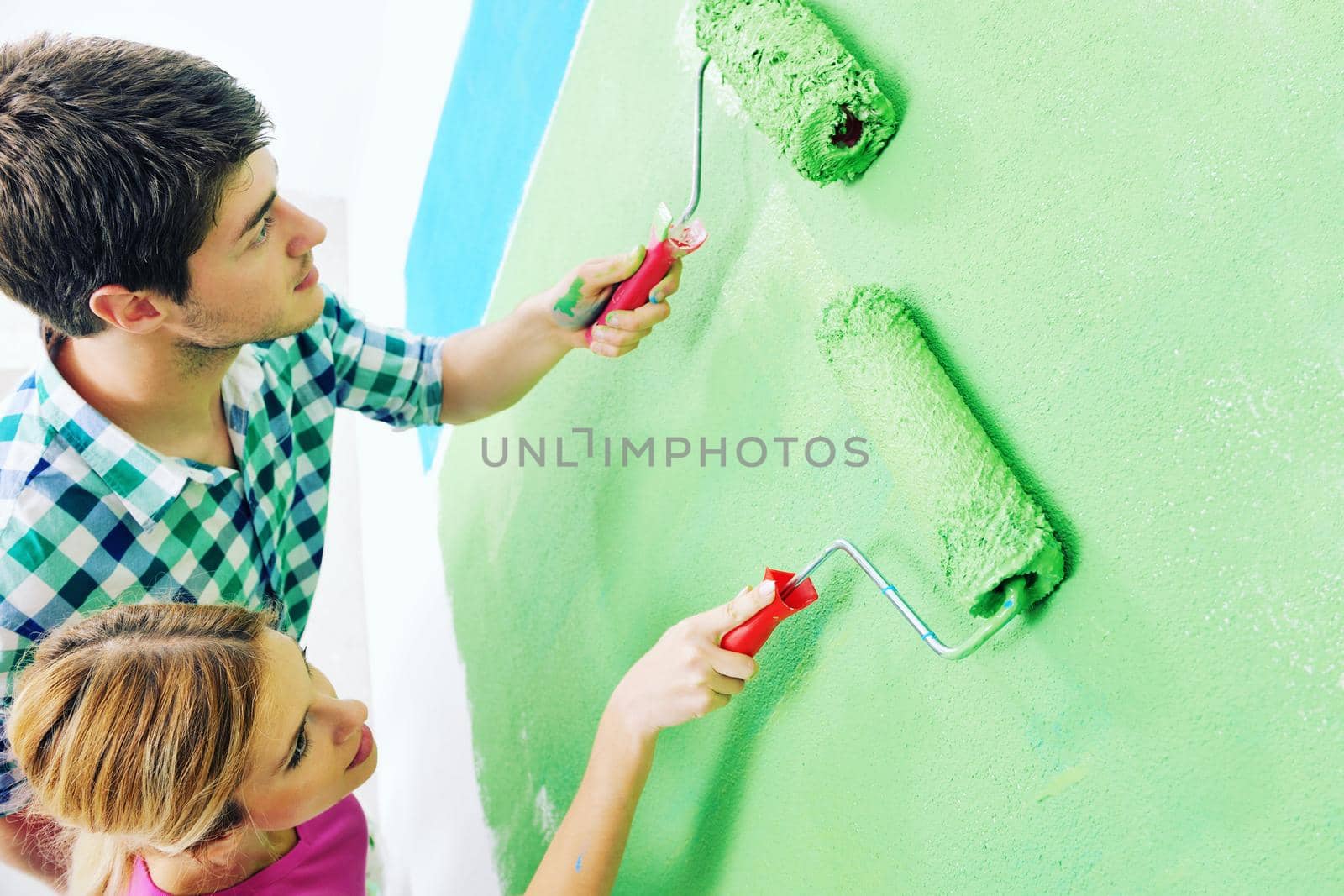 happy young couple paint in green and blue color white wall of their new home