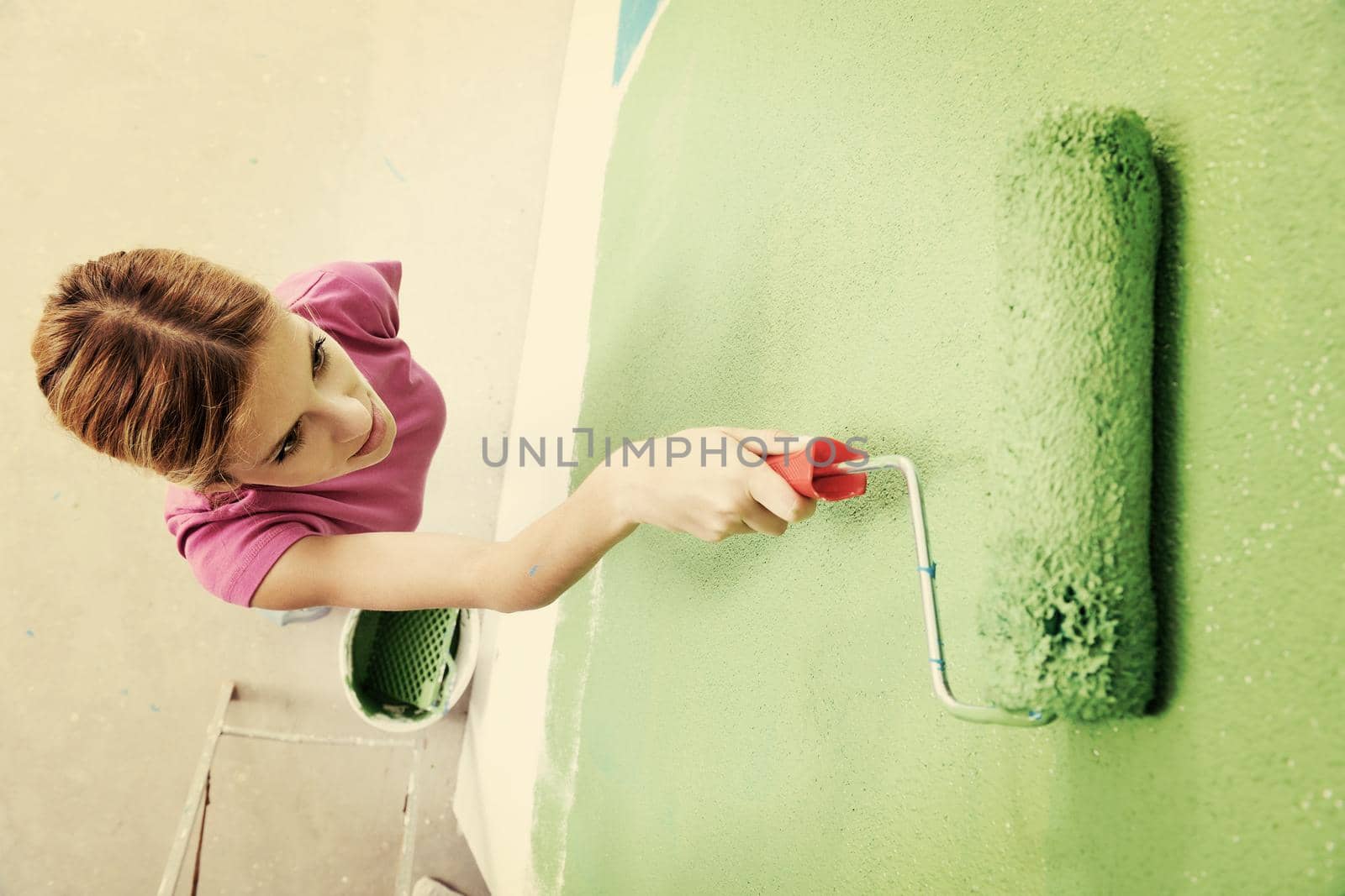 happy smiling woman painting interior white  wall in blue and green color of new house