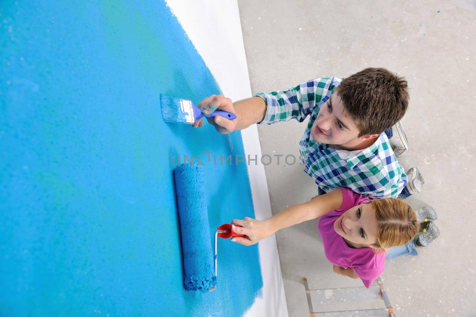 happy young couple paint in green and blue color white wall of their new home