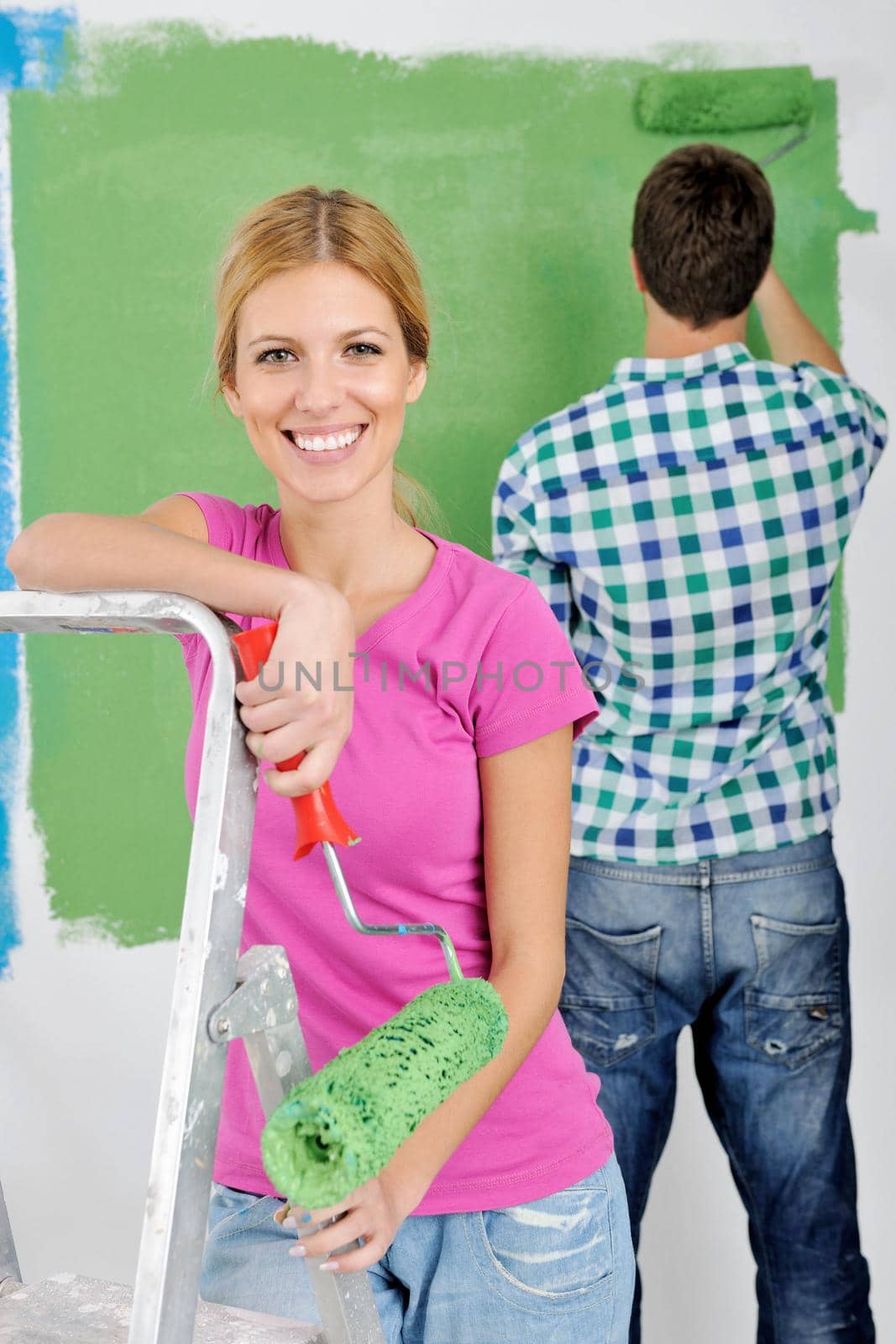 happy young couple paint in green and blue color white wall of their new home