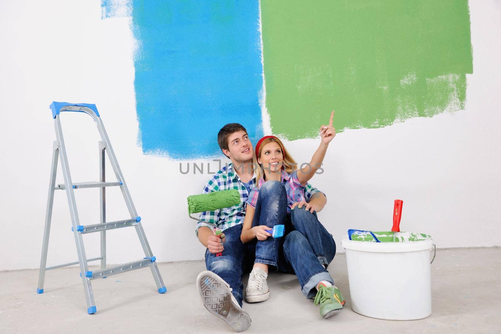 happy young couple relax after painting white wall in green and blue color in their new home