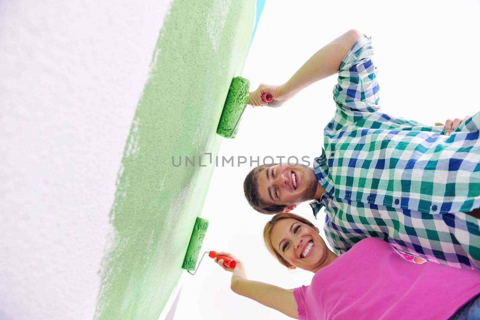 happy young couple paint in green and blue color white wall of their new home