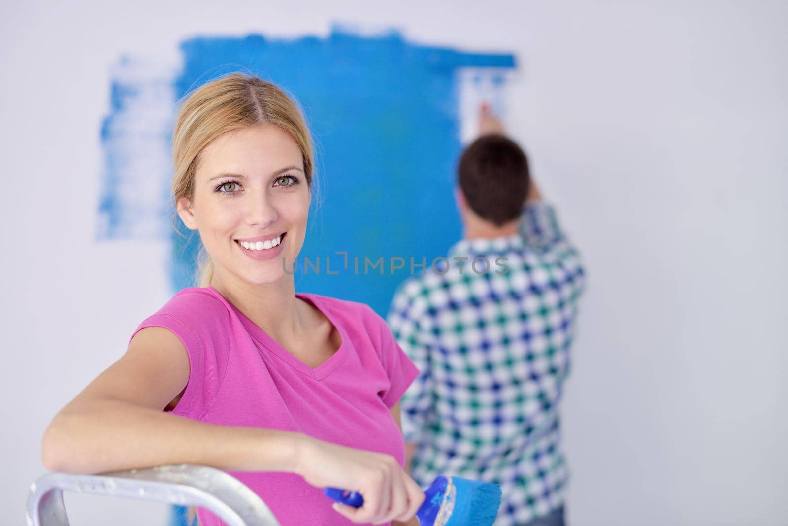 happy young couple paint in green and blue color white wall of their new home