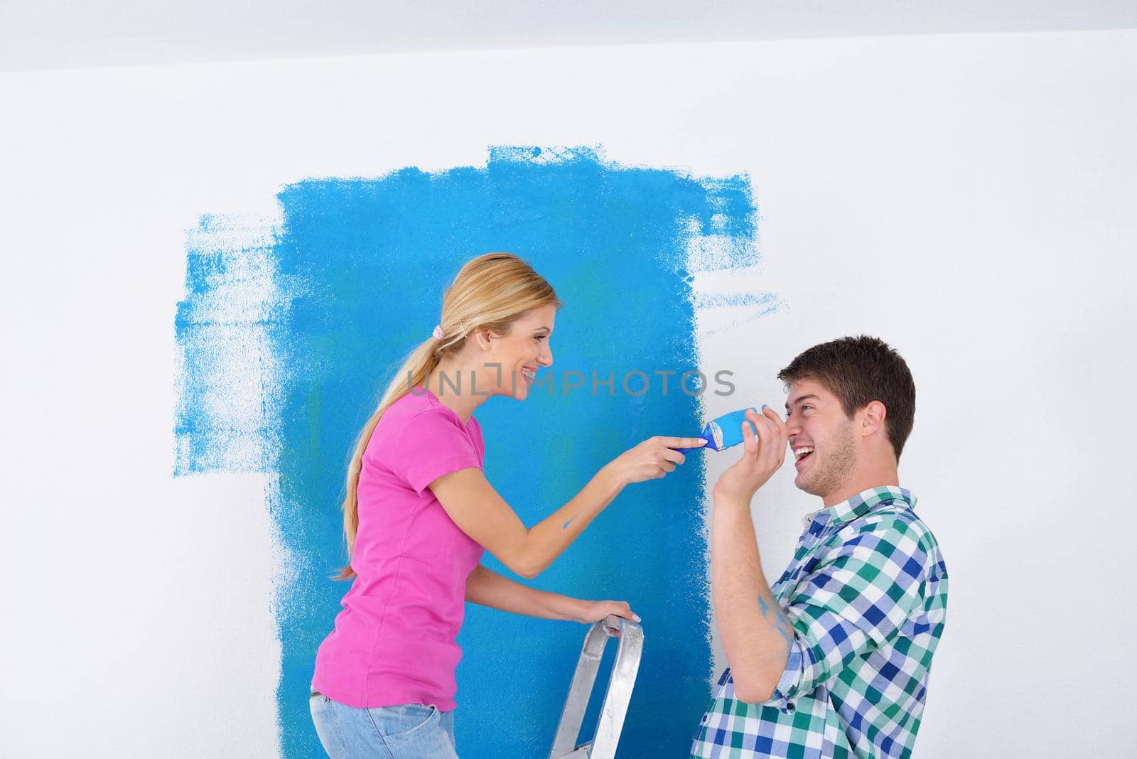 happy young couple paint in green and blue color white wall of their new home