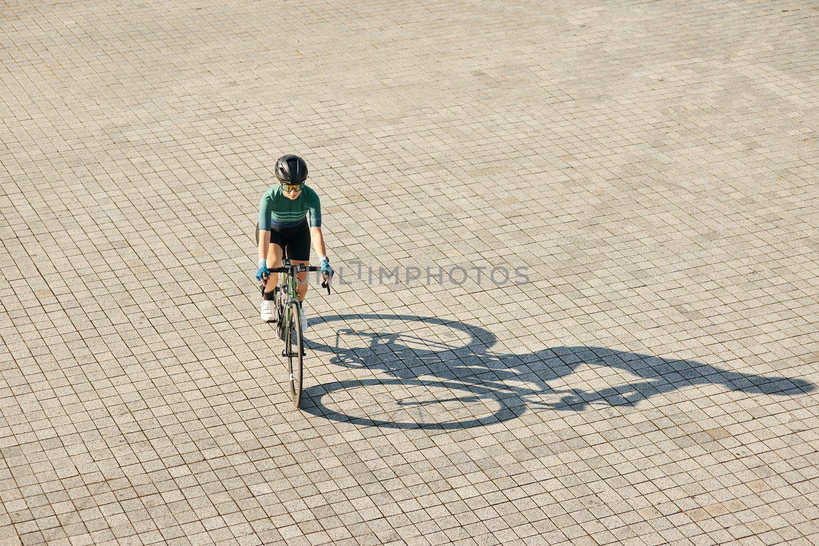 Aerial view shot of professional female cyclist in cycling garment and protective gear riding bicycle, training outdoors on a warm sunny day by friendsstock