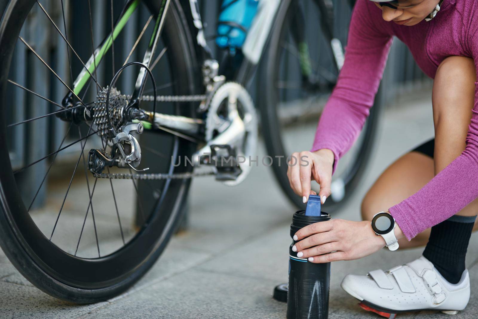 Cropped shot of young woman, professional female cyclist taking pump for inflating the tire of her bicycle, kneeling outdoors on a daytime by friendsstock