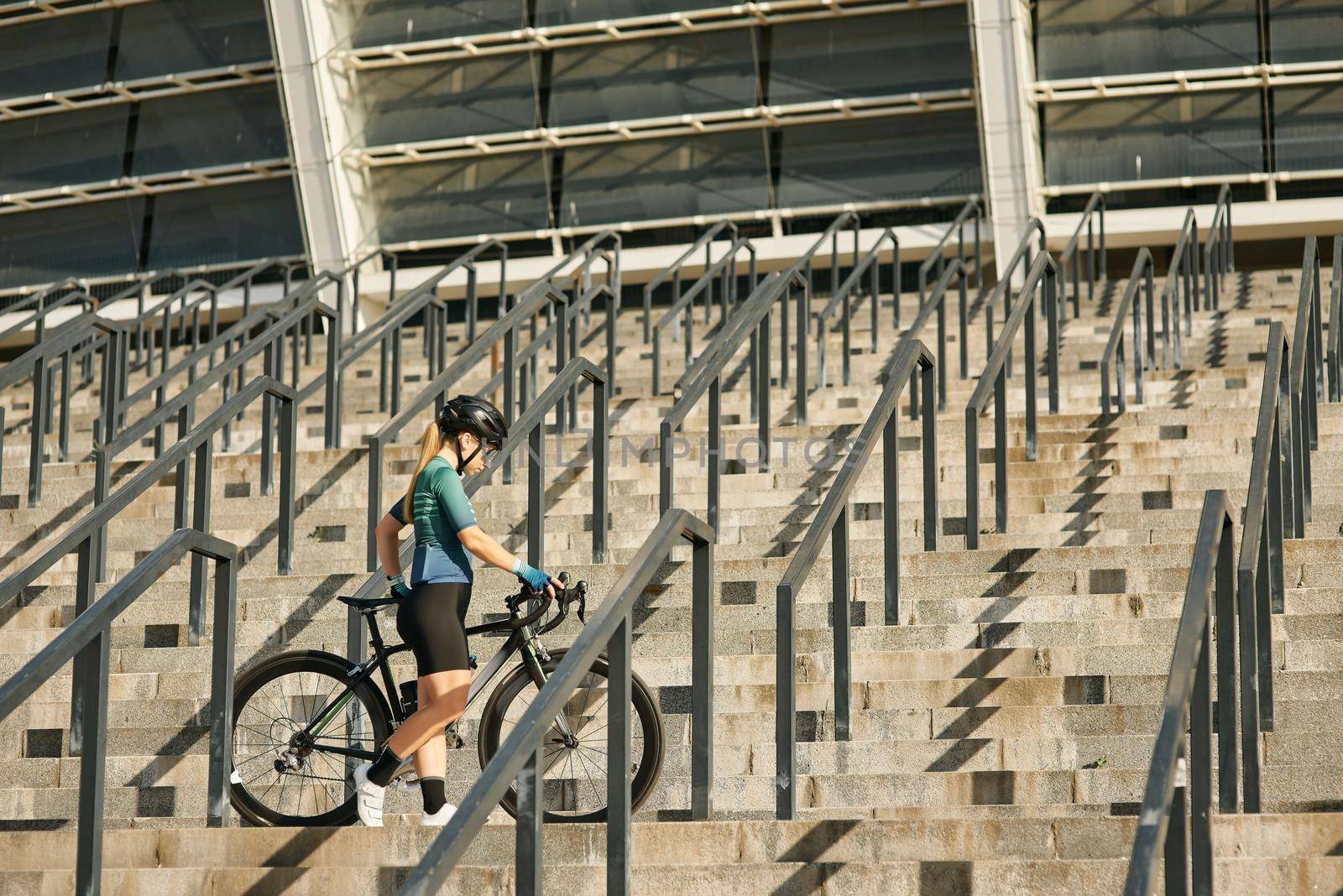 Young professional female cyclist in cycling garment and protective gear standing on the steps with her bike while exercising outdoors by friendsstock