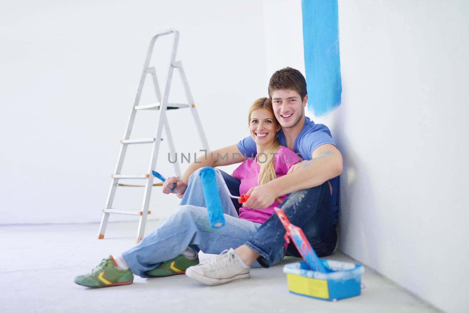 happy young couple relax after painting white wall in green and blue color in their new home