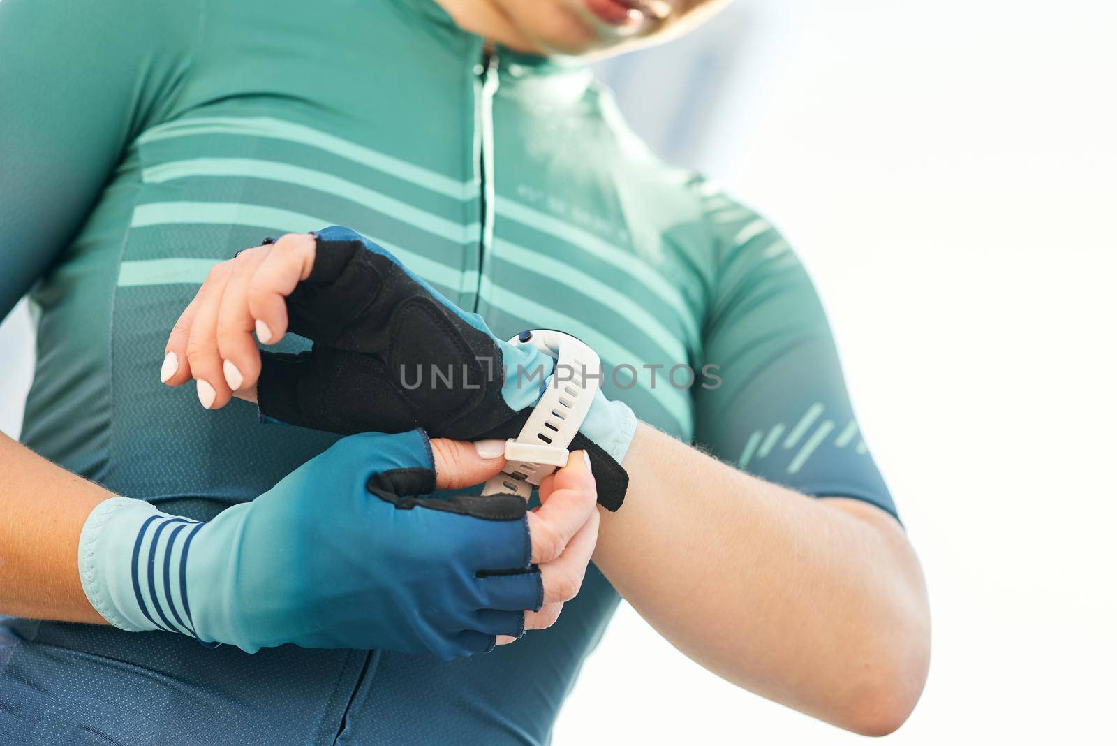 Cropped shot of professional female cyclist in sportswear putting on smart watch and cycling gloves while getting ready for training. Sports, extreme and active lifestyle concept