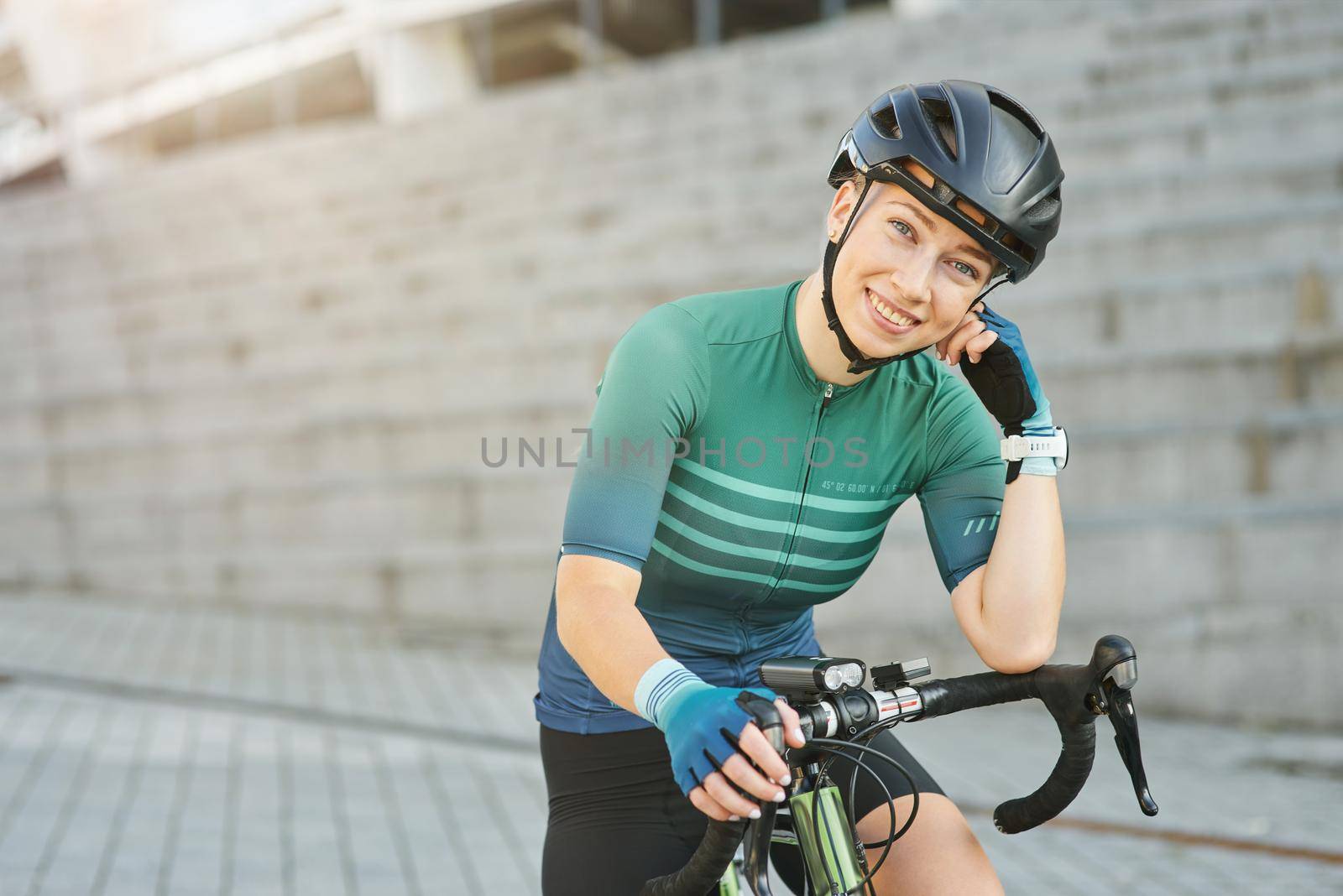Happy professional female cyclist in protective gear smiling at camera while standing with her bike outdoors on a daytime. Active lifestyle, sports concept