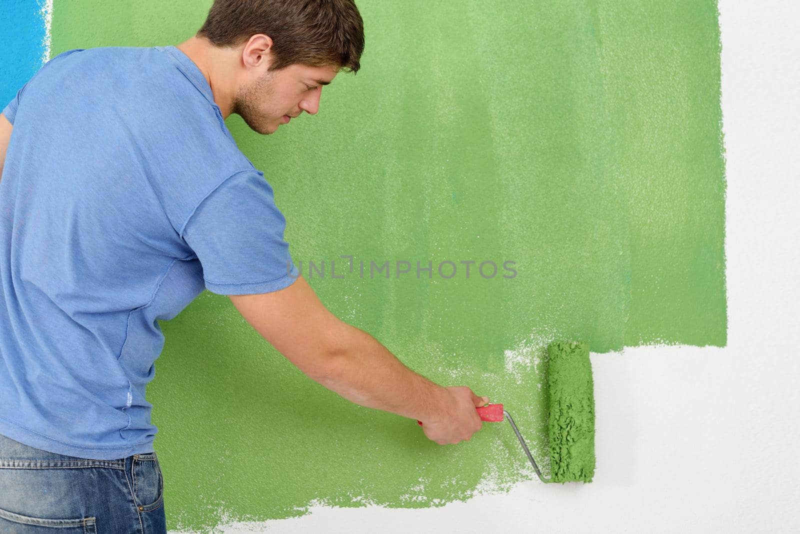 handsome young man paint in blue and green color  white wall of new home