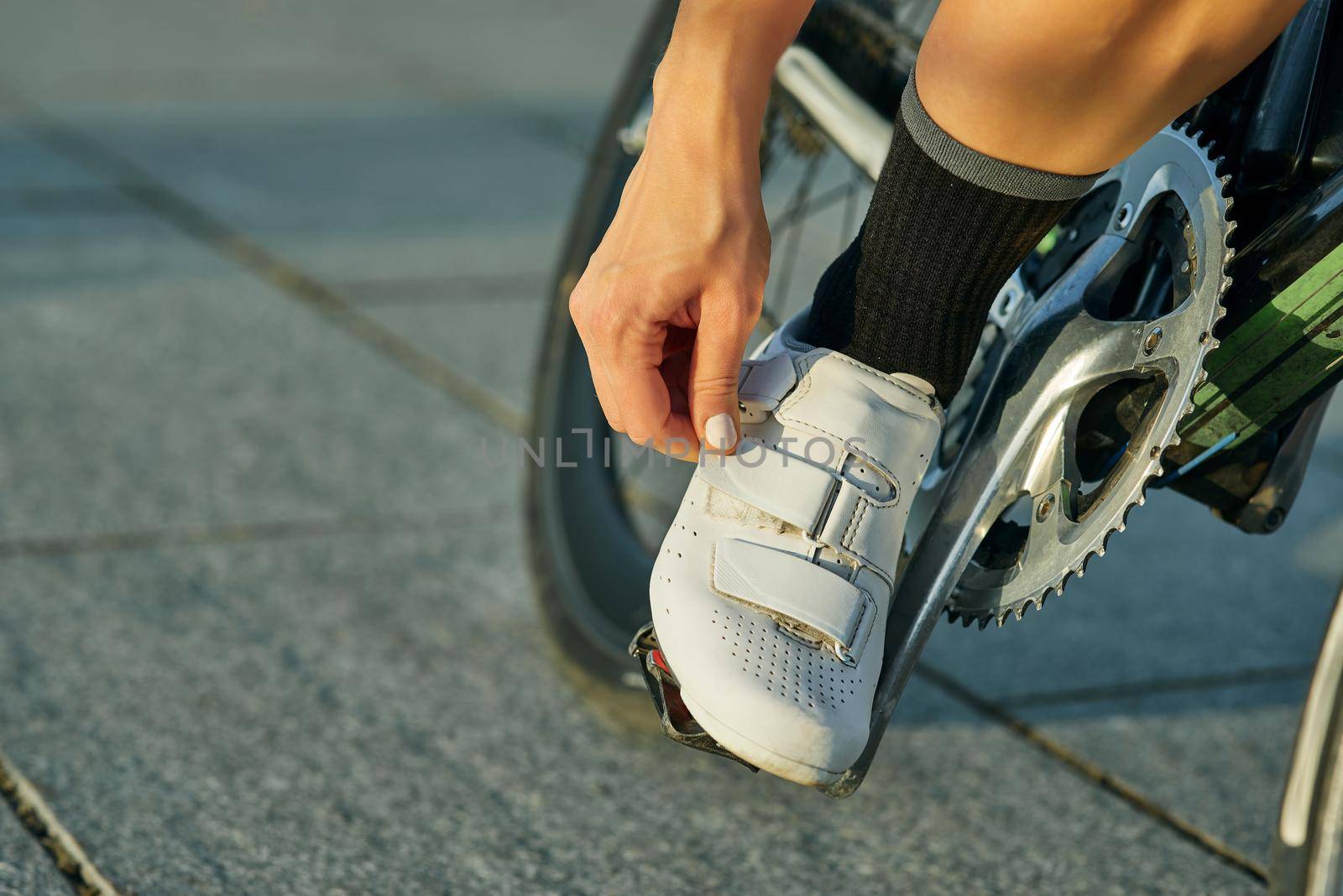 Close up shot of female cyclist wearing, fastening cycling shoes while riding bike, training outdoors on a warm day. Active lifestyle, sports concept