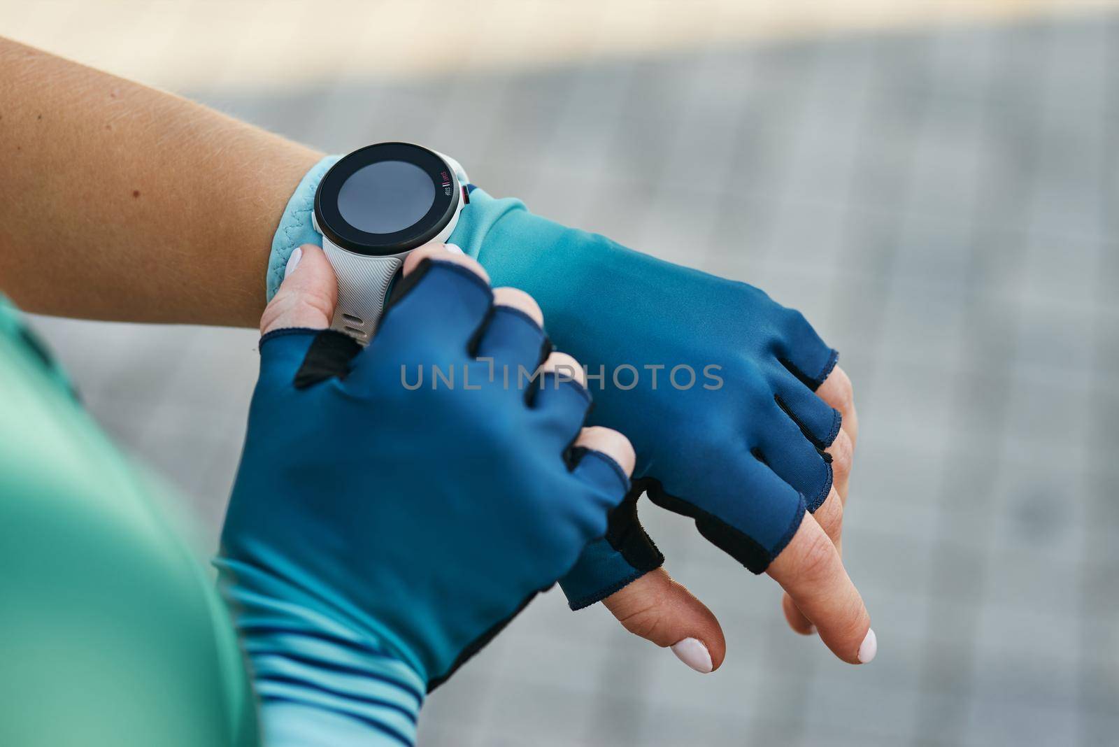 Closeup shot of hands of professional female cyclist in sportswear putting on smart watch while getting ready for training. Sports, extreme and active lifestyle concept