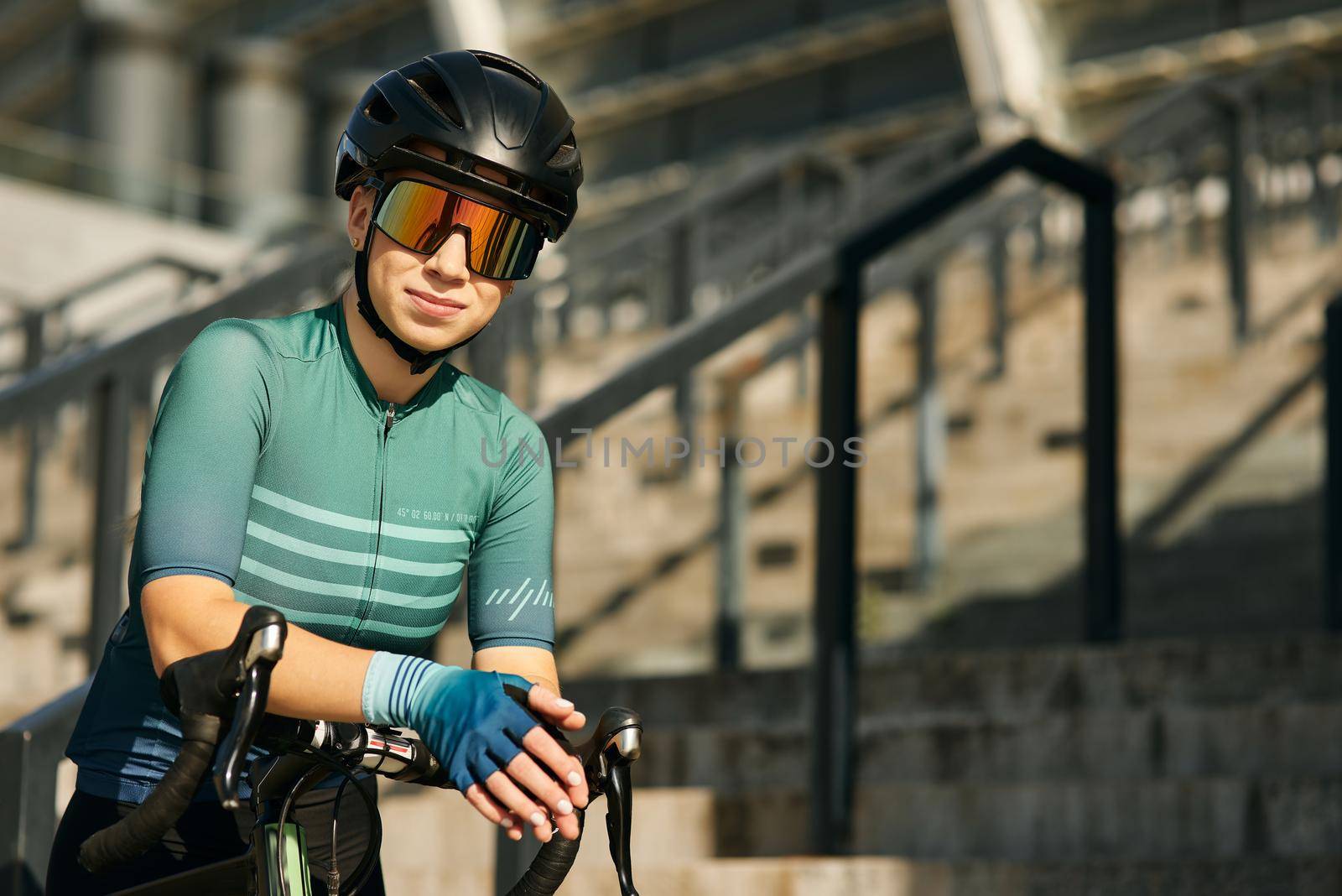Portrait of professional female cyclist in cycling garment and protective gear posing for camera while having a training, riding bicycle in city center by friendsstock