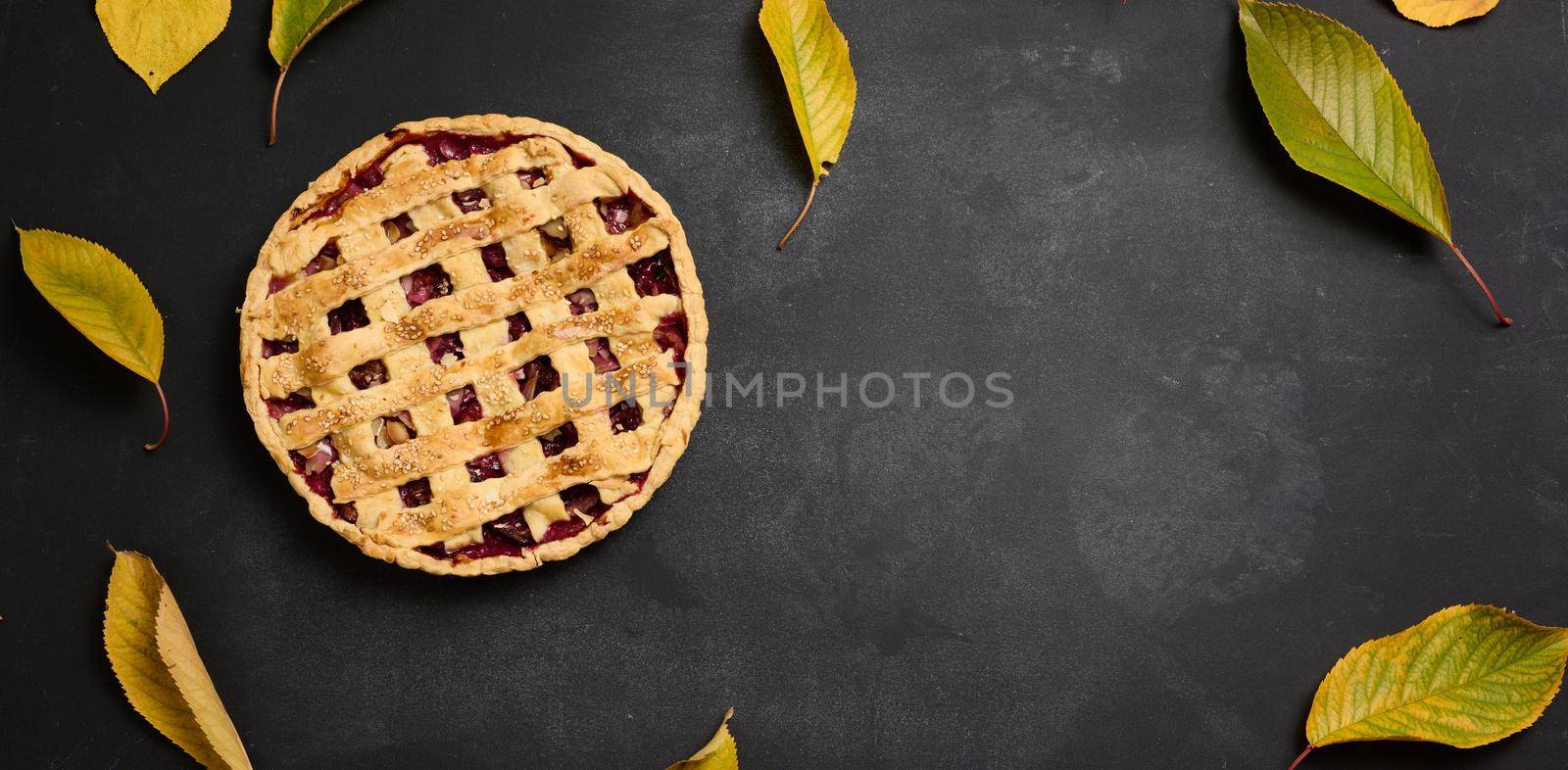 baked round pie with plums on a black background, top view. Place for inscription