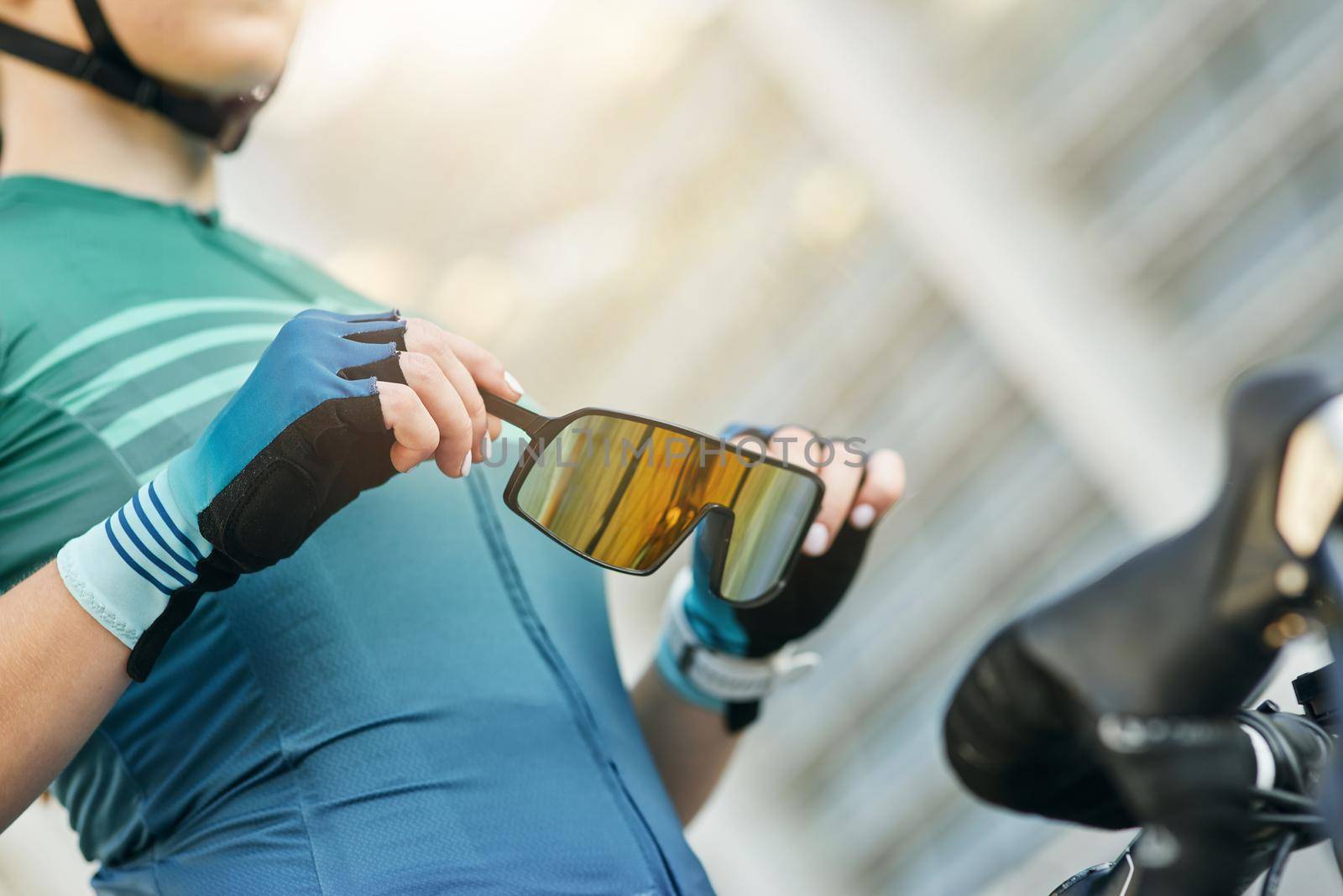 Close up of hands of professional female cyclist holding and putting on protective glasses while getting ready for training outdoors by friendsstock