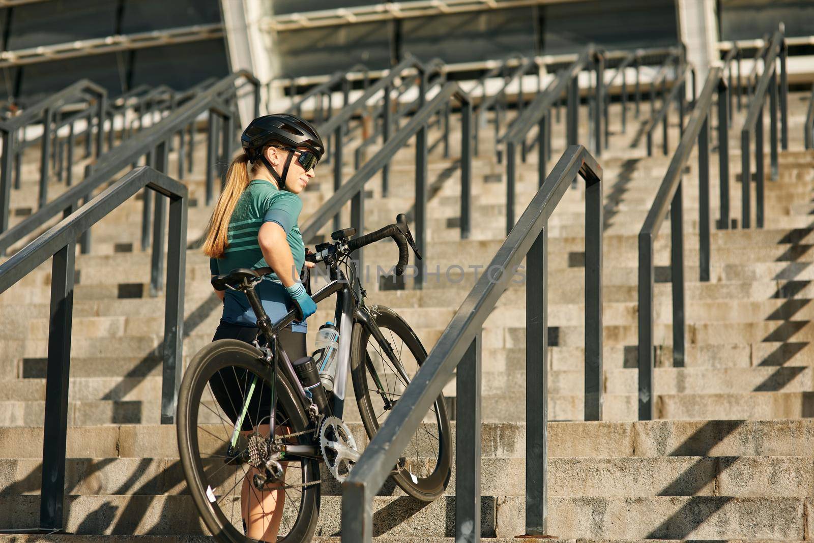 Sportive young woman, professional female cyclist looking away while coming up the steps with bicycle, training outdoors. Sports, active lifestyle concept