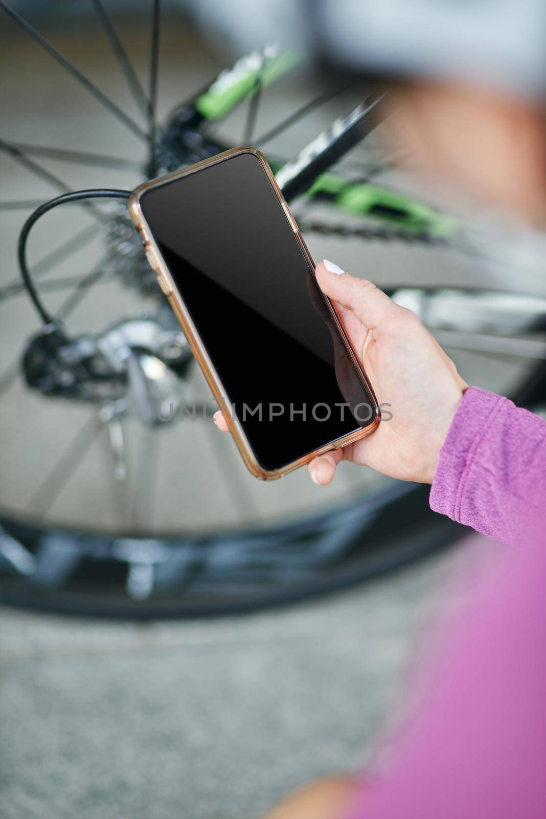 Close up shot of hand of female cyclist holding smartphone while checking her bicycle mechanisms, sprocket and chain on a mountain bike outdoors on a daytime. Safety, sports, technology concept