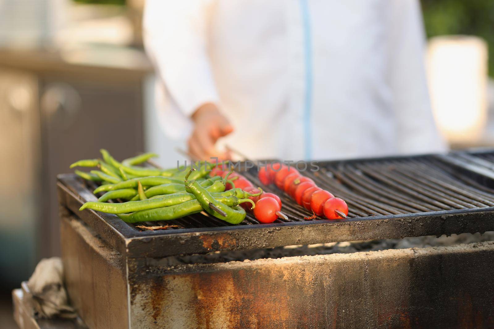 Amateur chef frying fresh tomatoes and green pepper on grill on open air by kuprevich