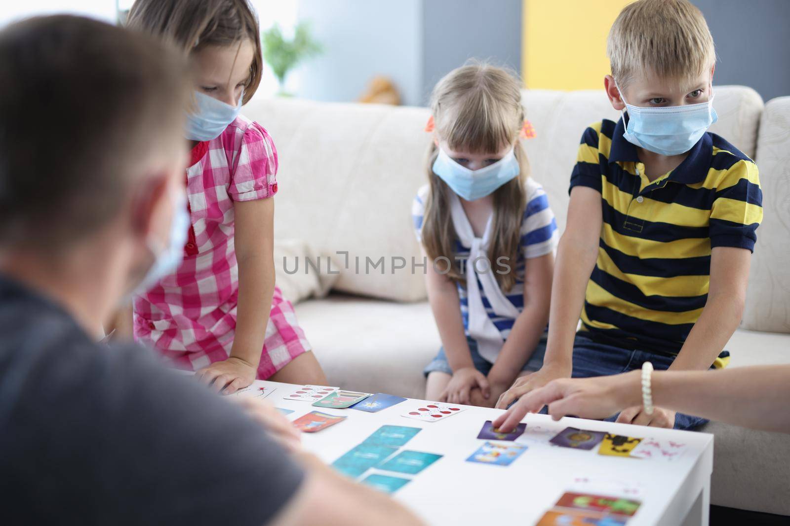 Portrait of children wearing face mask, virus spread in kindergarten, friends got sick. Kids playing card game with adults. Coronavirus, quarantine concept