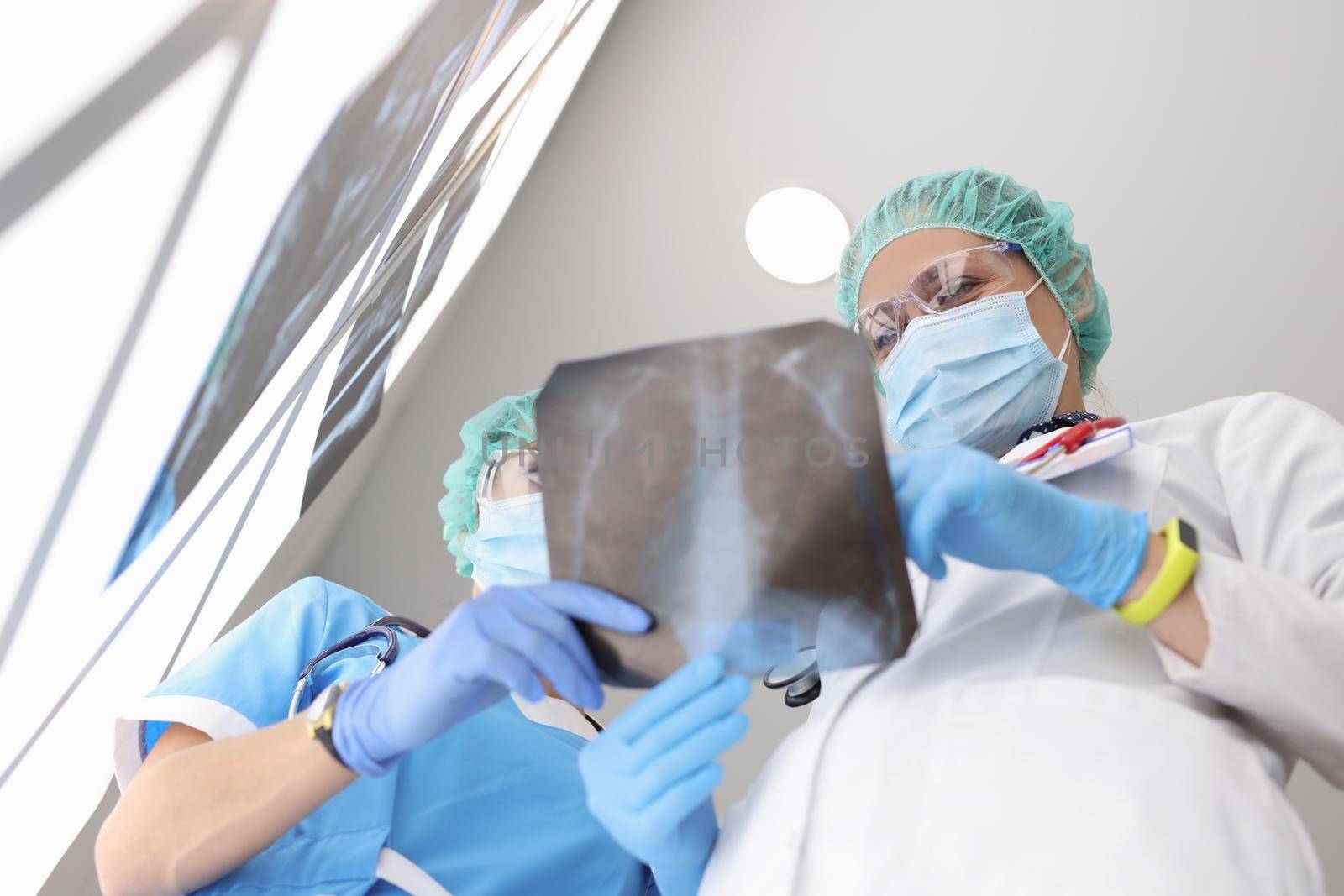 Low angle of medical workers examine x ray of patient lungs, colleagues discuss scan result. Doctor lungs scan in clinic. Checkup, coronavirus concept