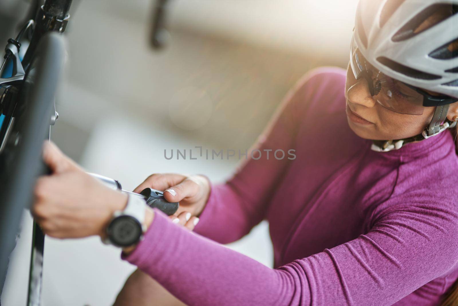 Professional female cyclist wearing protective helmet and glasses looking focused, using pump for inflating the tire of her bicycle, kneeling outdoors on a daytime. Transportation, sports concept