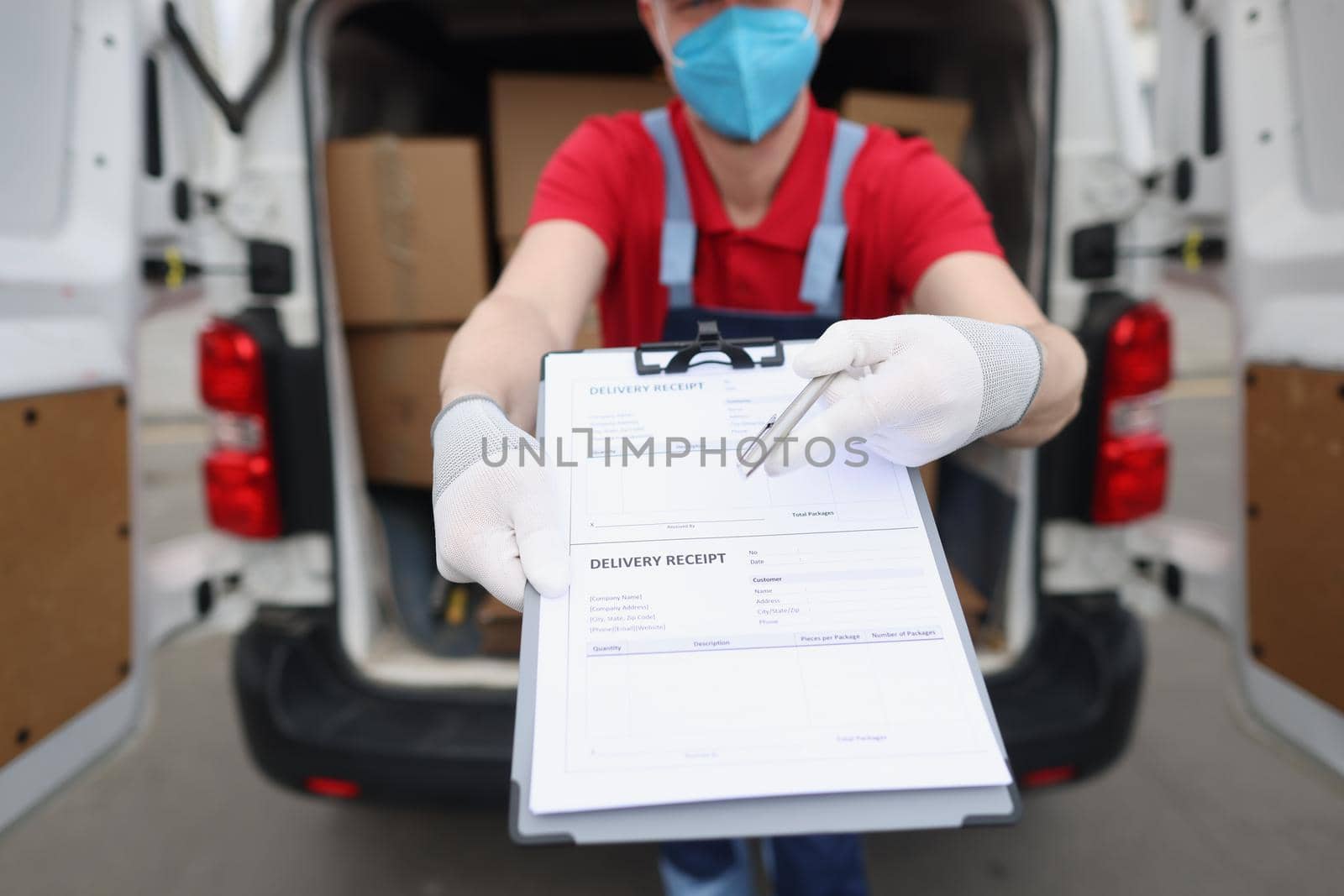 Man in uniform and face mask give delivery receipt paper to receiver to sign by kuprevich