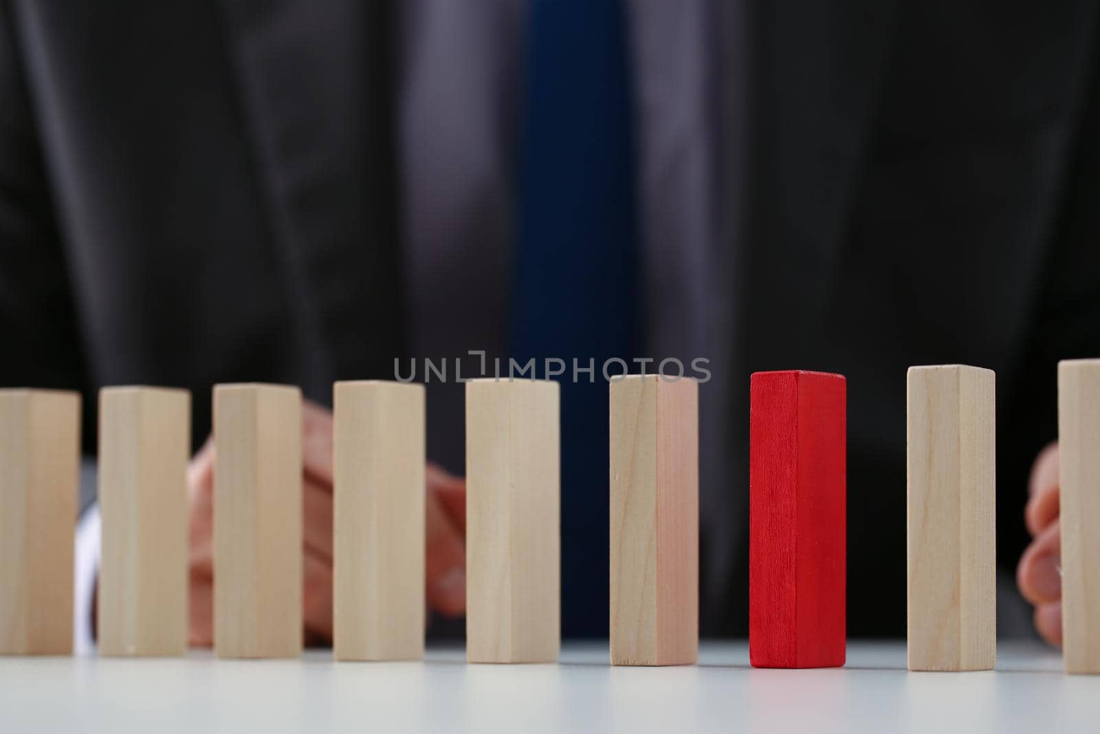 Close-up of businessman choose red wood block over simple similar wooden cubes. Dominos stand in line row. Business organization, startup, leader concept