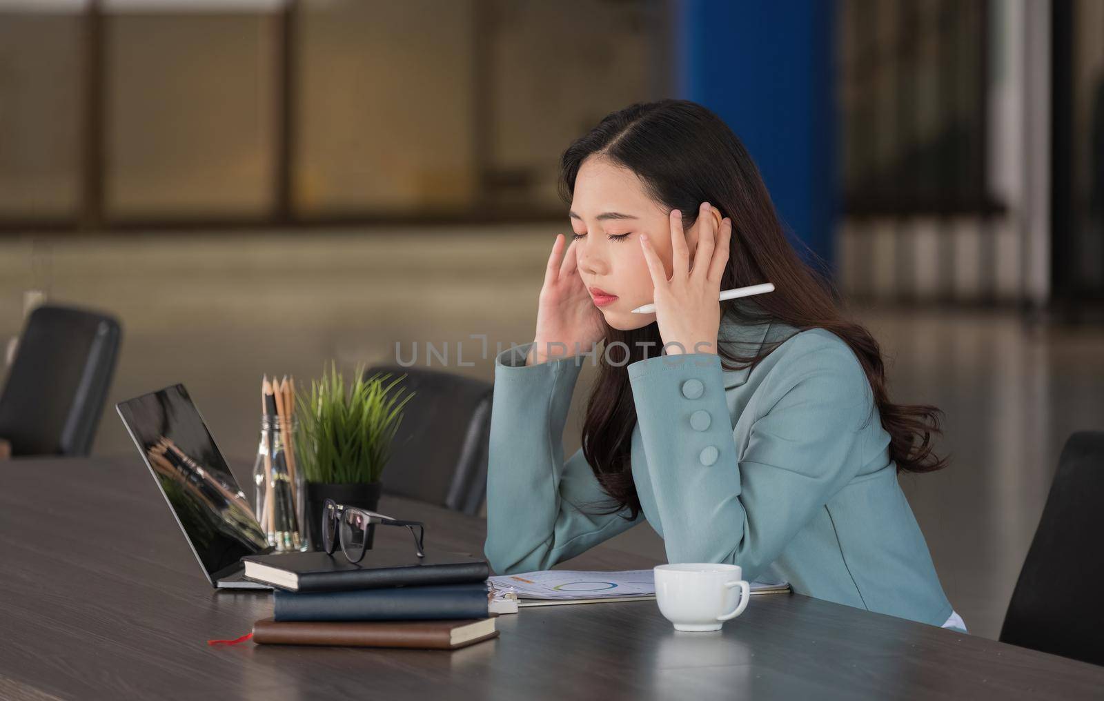 Tired business asian woman with headache looking uncomfortable while working with laptop computer in the office by nateemee