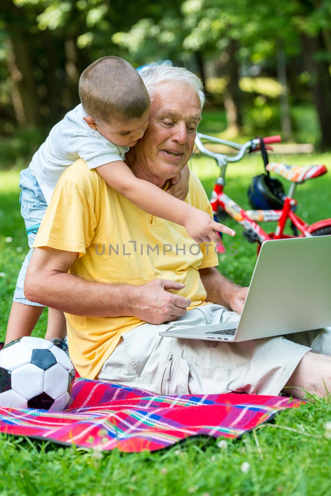 happy elderly senior grandfather and child in park using laptop computer