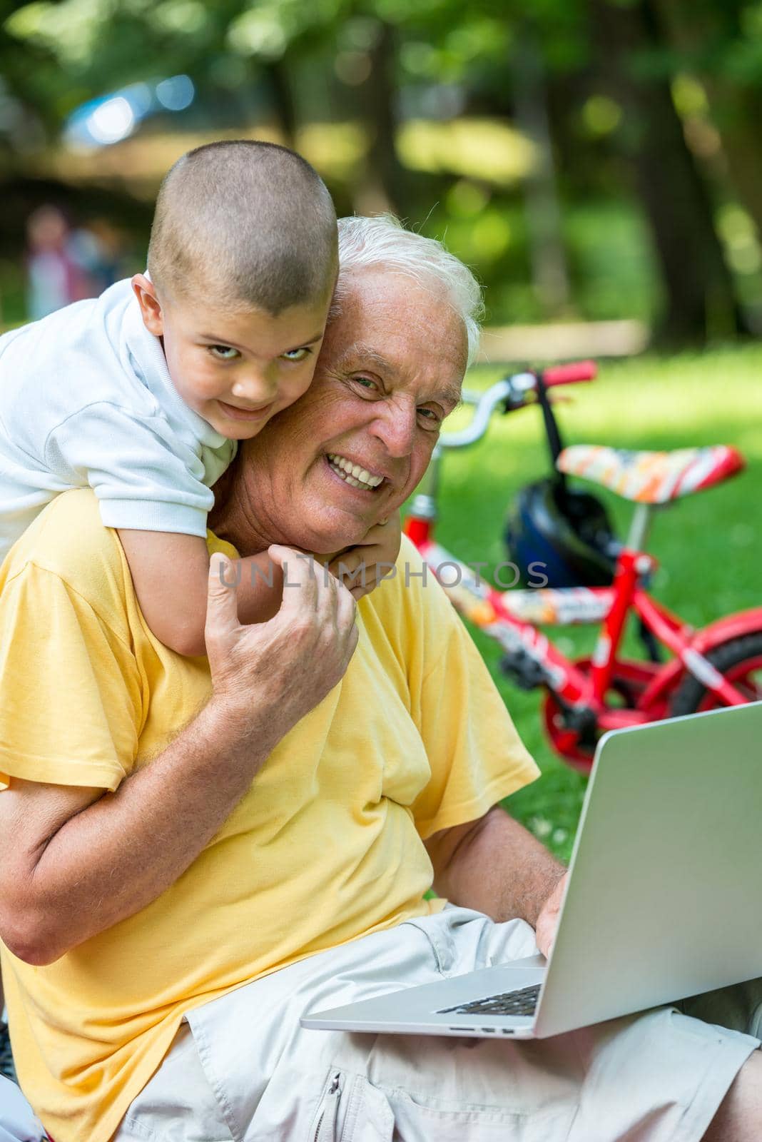 happy elderly senior grandfather and child in park using laptop computer