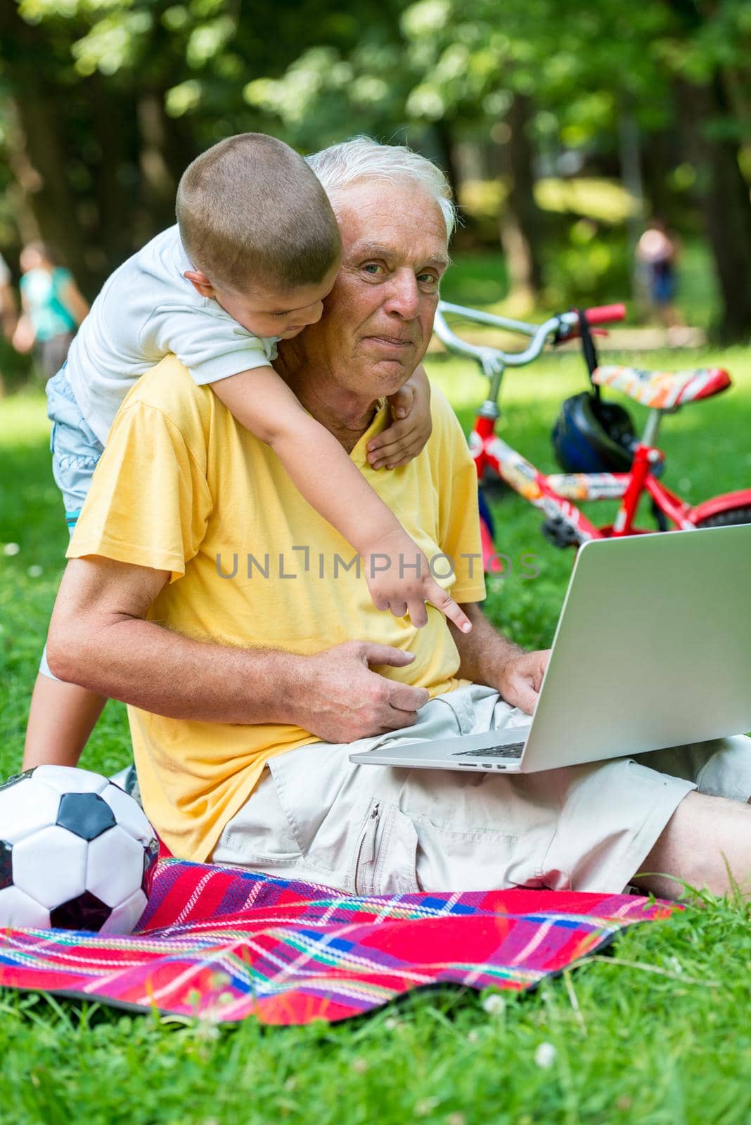 happy elderly senior grandfather and child in park using laptop computer