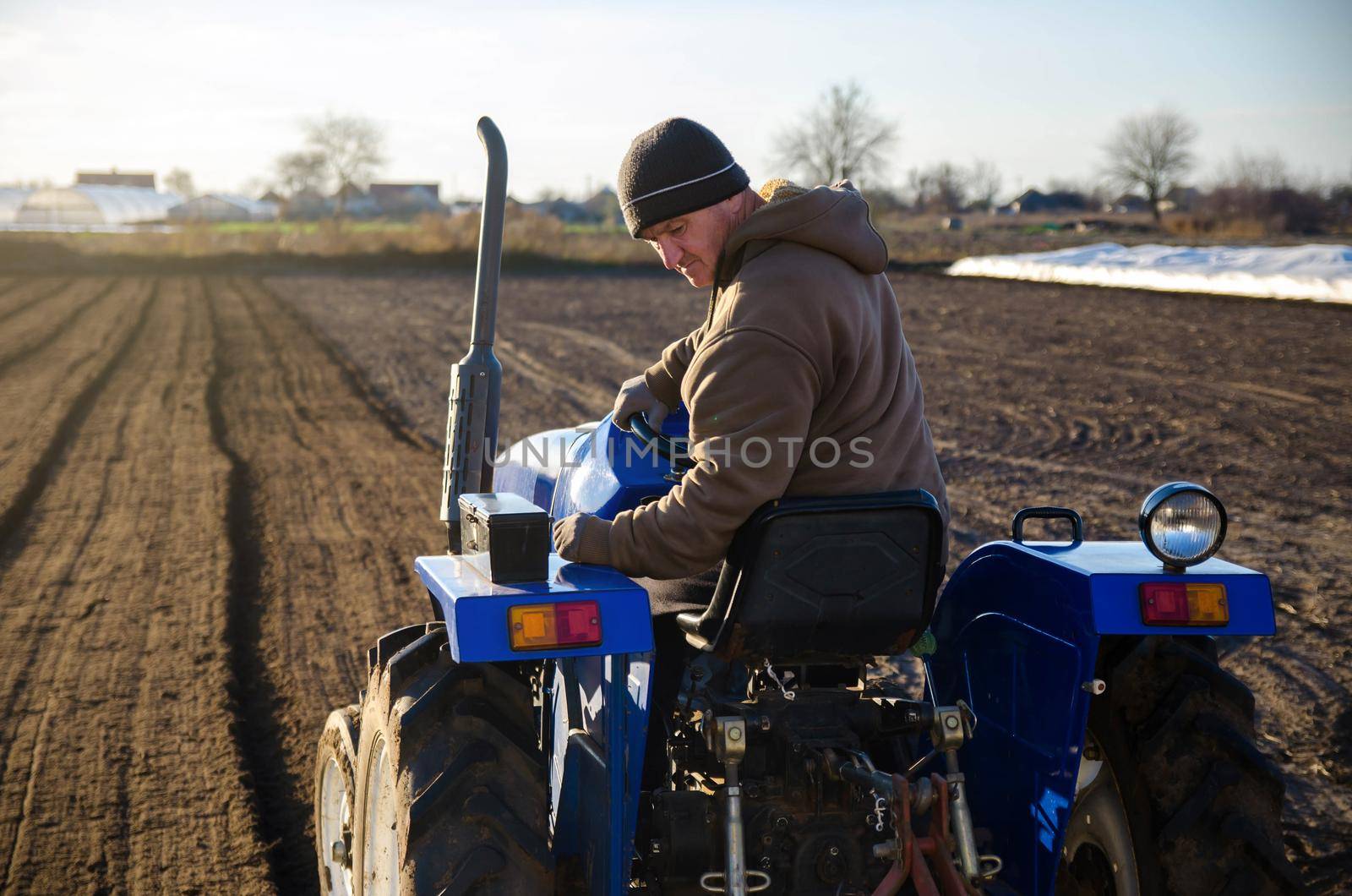 Senior farmer cultivating the farm field on a tractor. Seasonal worker. Recruiting workers for work on agricultural machinery. Land cultivation. Farming. Small farms. Rural scene. Farm business by iLixe48