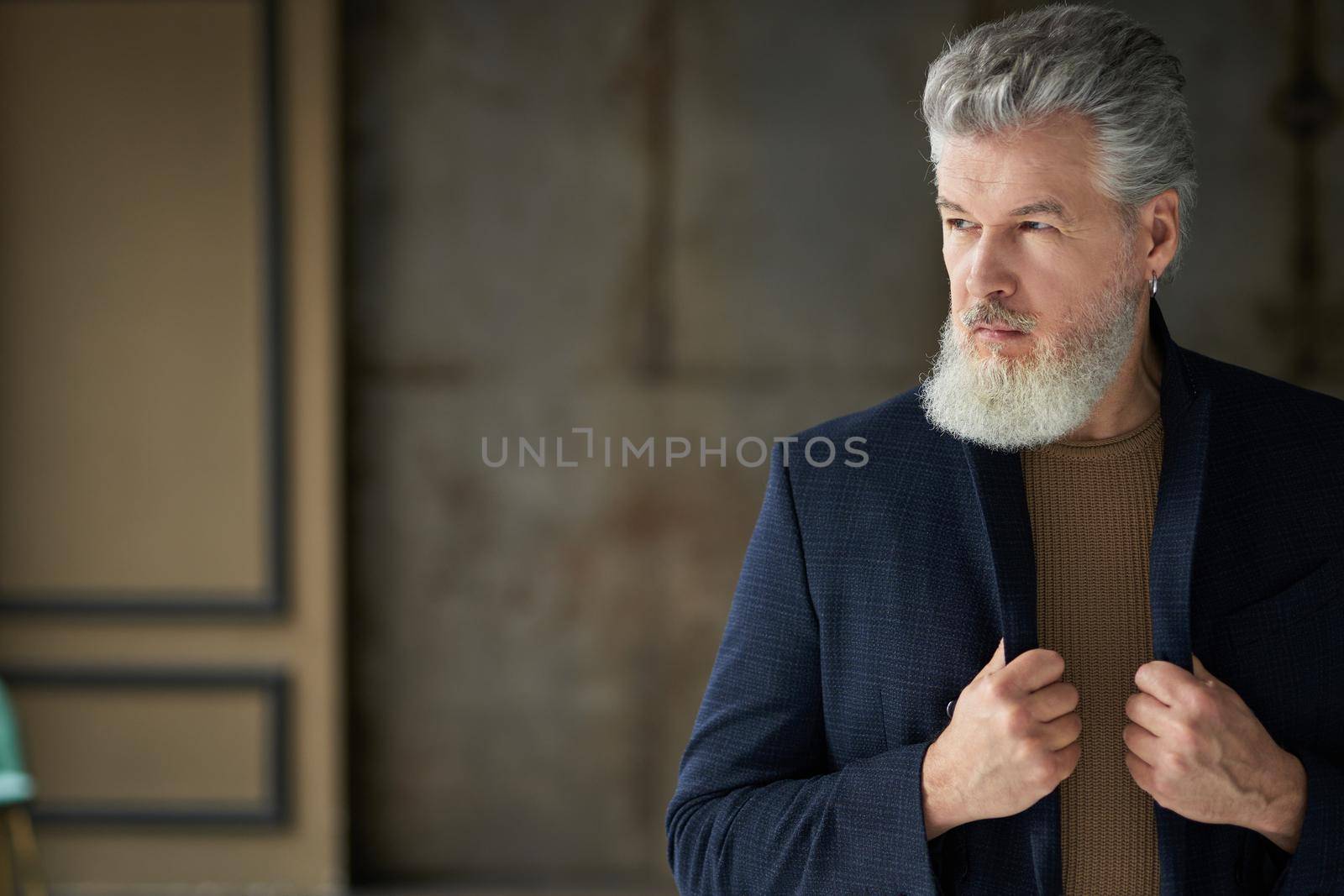 Stylish serious handsome middle aged man looking away, adjusting his suit while posing indoors by friendsstock