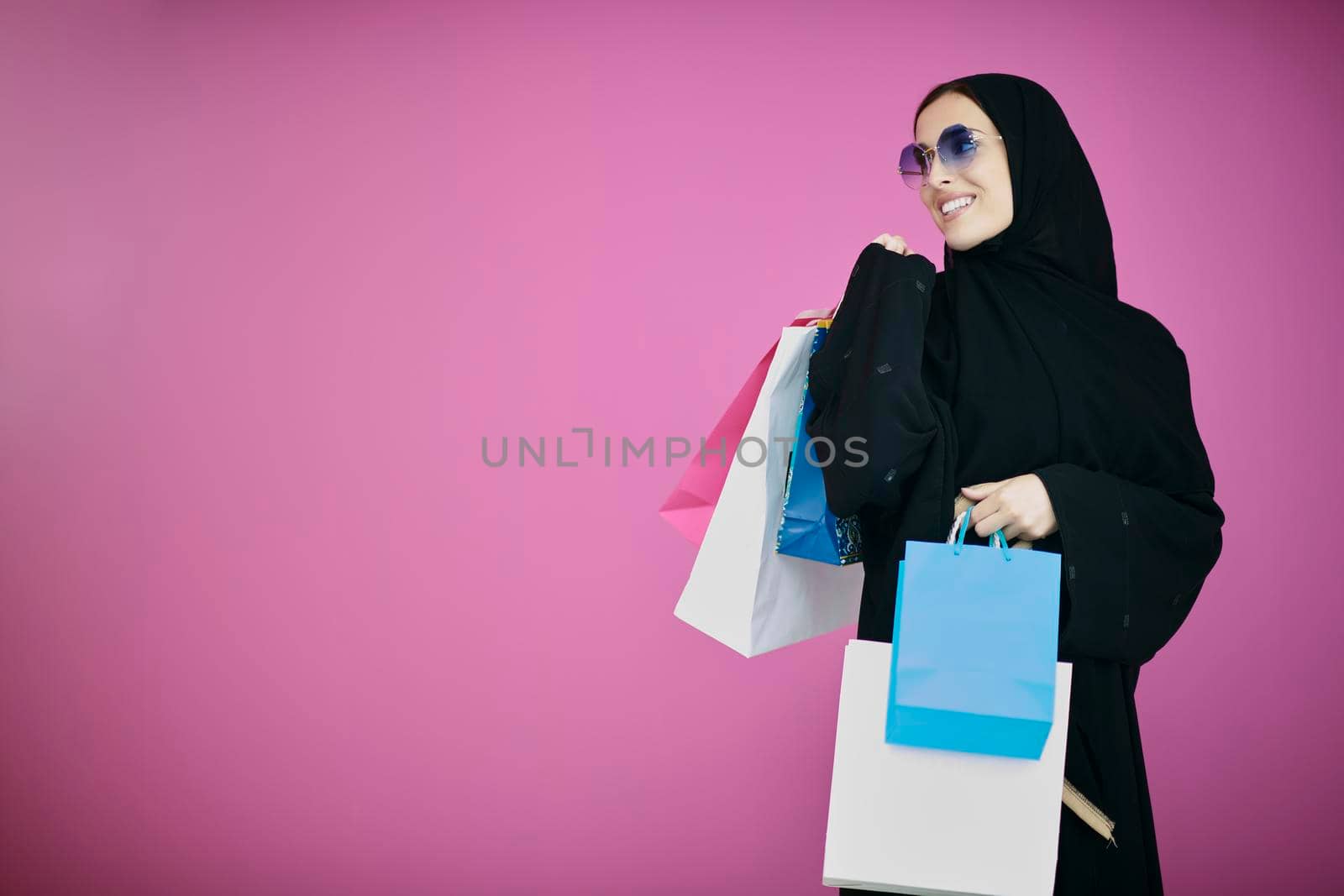 Happy muslim girl posing with shopping bags. Arabic woman wearing traditional black clothes and sunglasses representing rich and  luxurious lifestyle