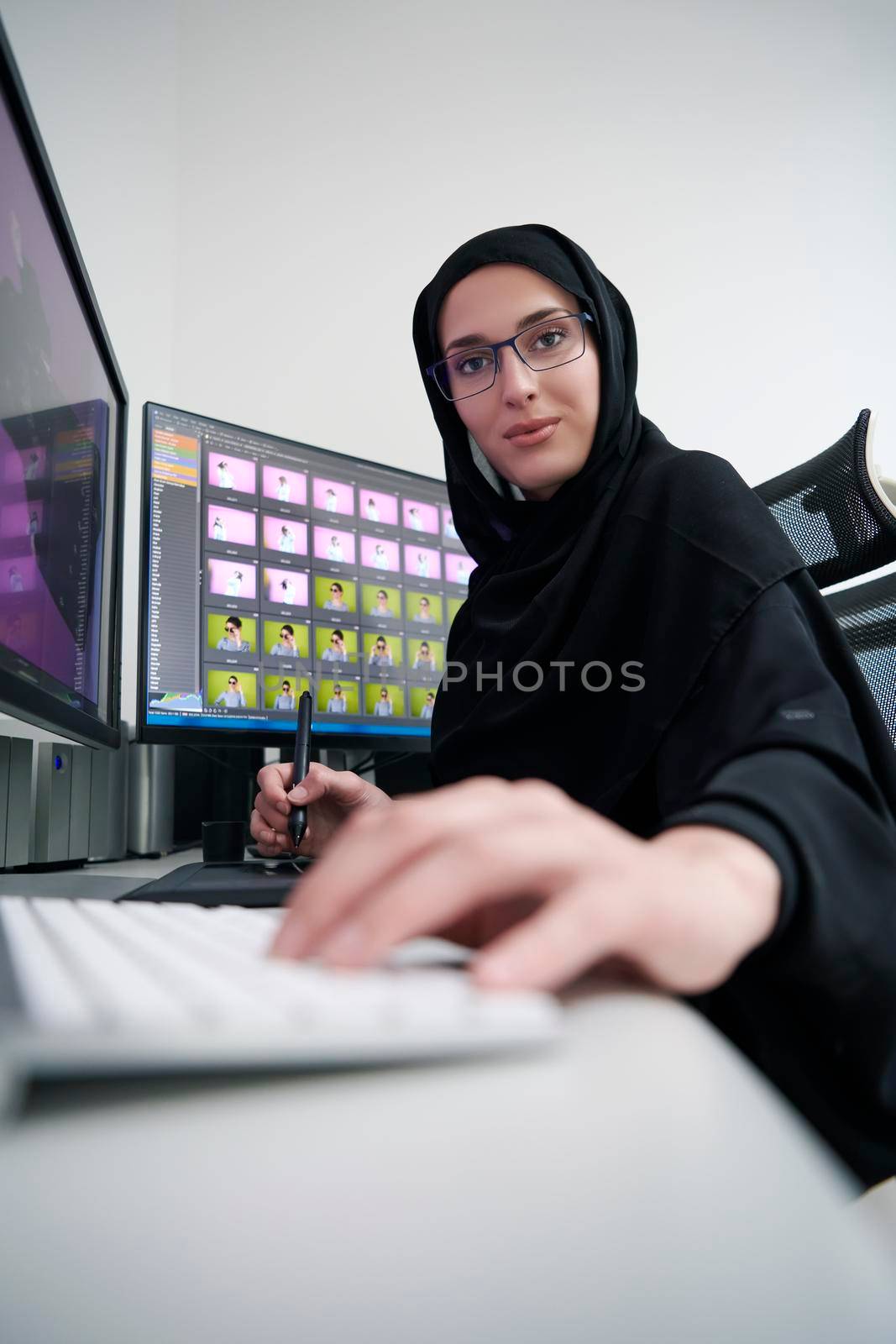 Muslim female graphic designer working on computer using graphic tablet and two monitors by dotshock