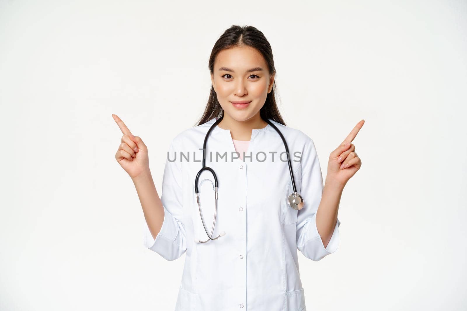 Portrait of asian female doctor, young healthcare worker in medical robe pointing sideways, showing two choices, both ways, white background.
