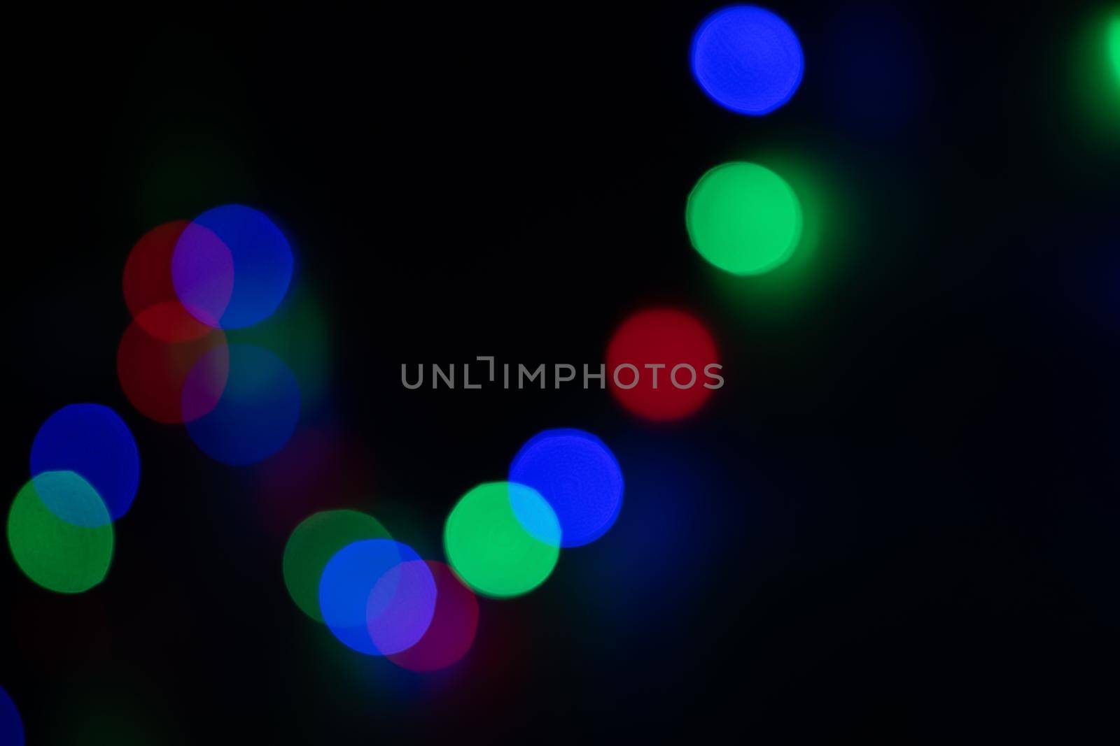 Defocused bokeh lights on black background, an abstract naturally blurred backdrop for Christmas eve or birthday party. Festive light texture. Colorful garland in blur. Overlay effect for design