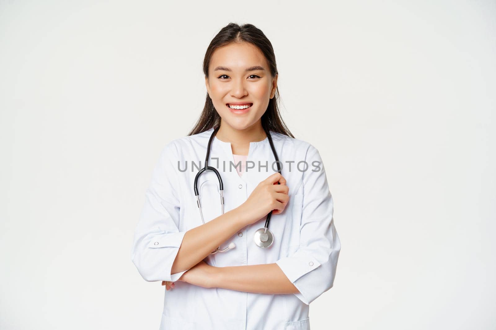 Healthcare and hospital concept. Smiling asian doctor, female nurse in uniform, looking happy at camera, standing over white background.