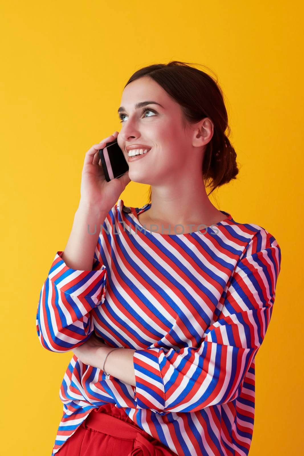 Portrait of young girl talking on the phone while standing in front of yellow background. Female model representing modern fashion and technology concept