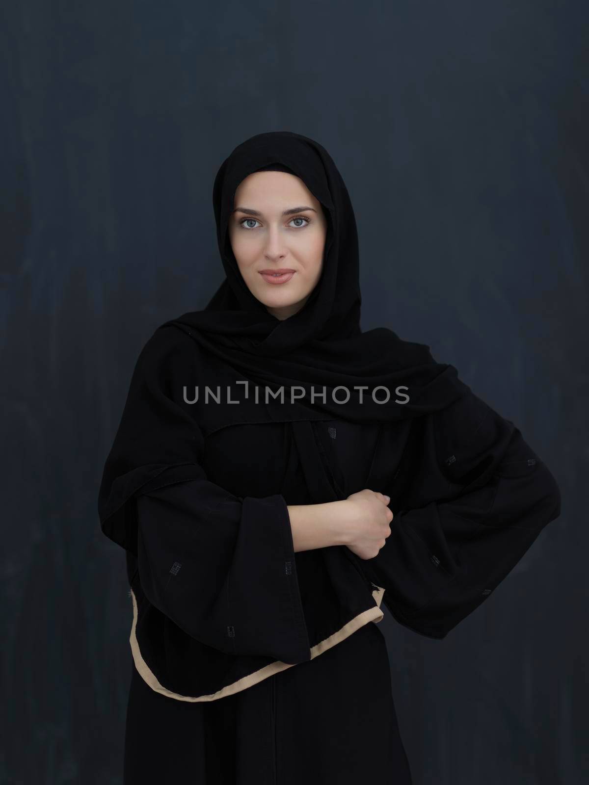 Portrait of modern young muslim woman in black abaya. Arab girl wearing traditional clothes and posing in front of black chalkboard. Representing modern and rich arabic lifestyle