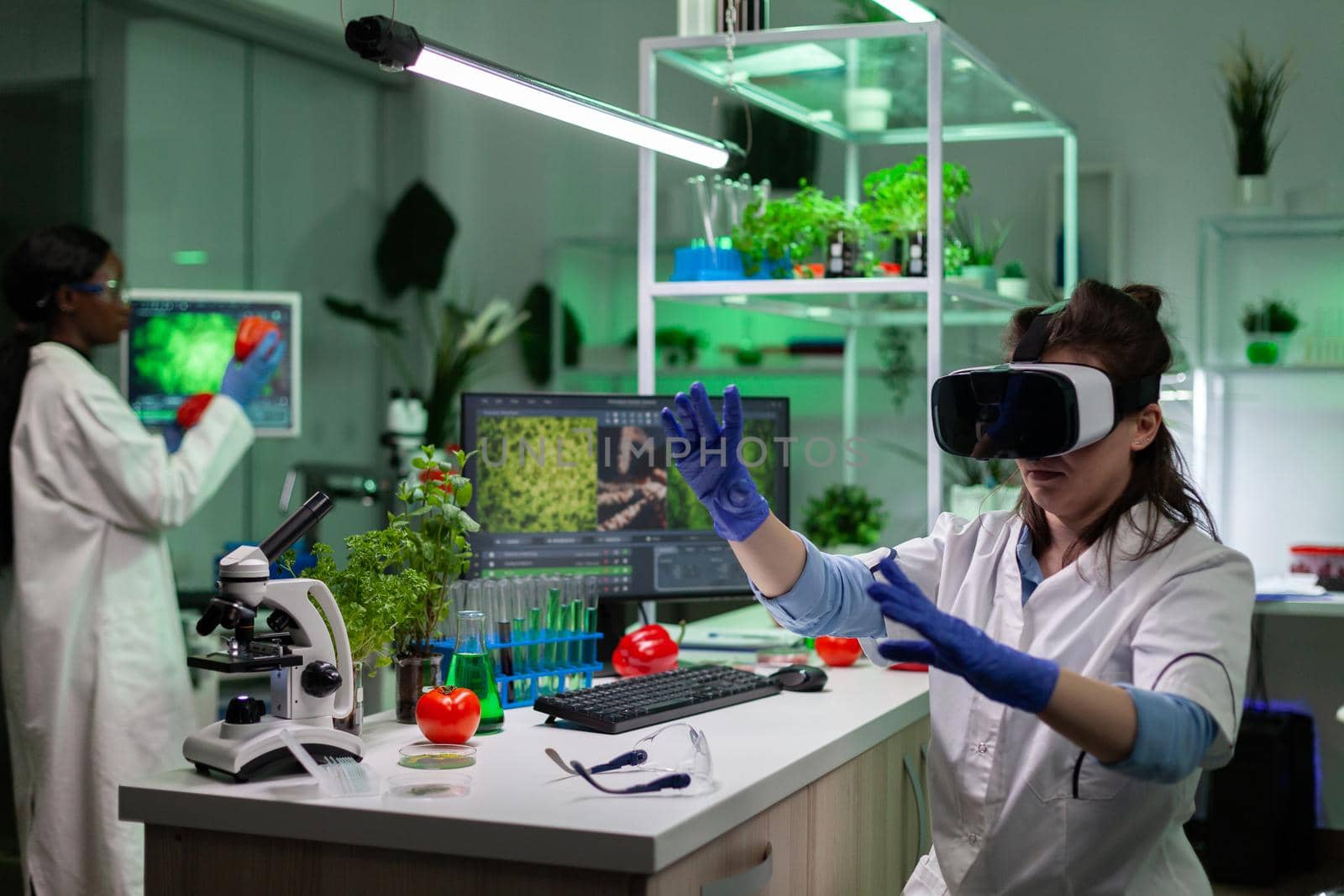 Chemist scientist doctor woman wearing virtual reality headphones analyzing microbiology experiment working in pharmaceutical hospital laboratory. Genetically modified plants of computer screen
