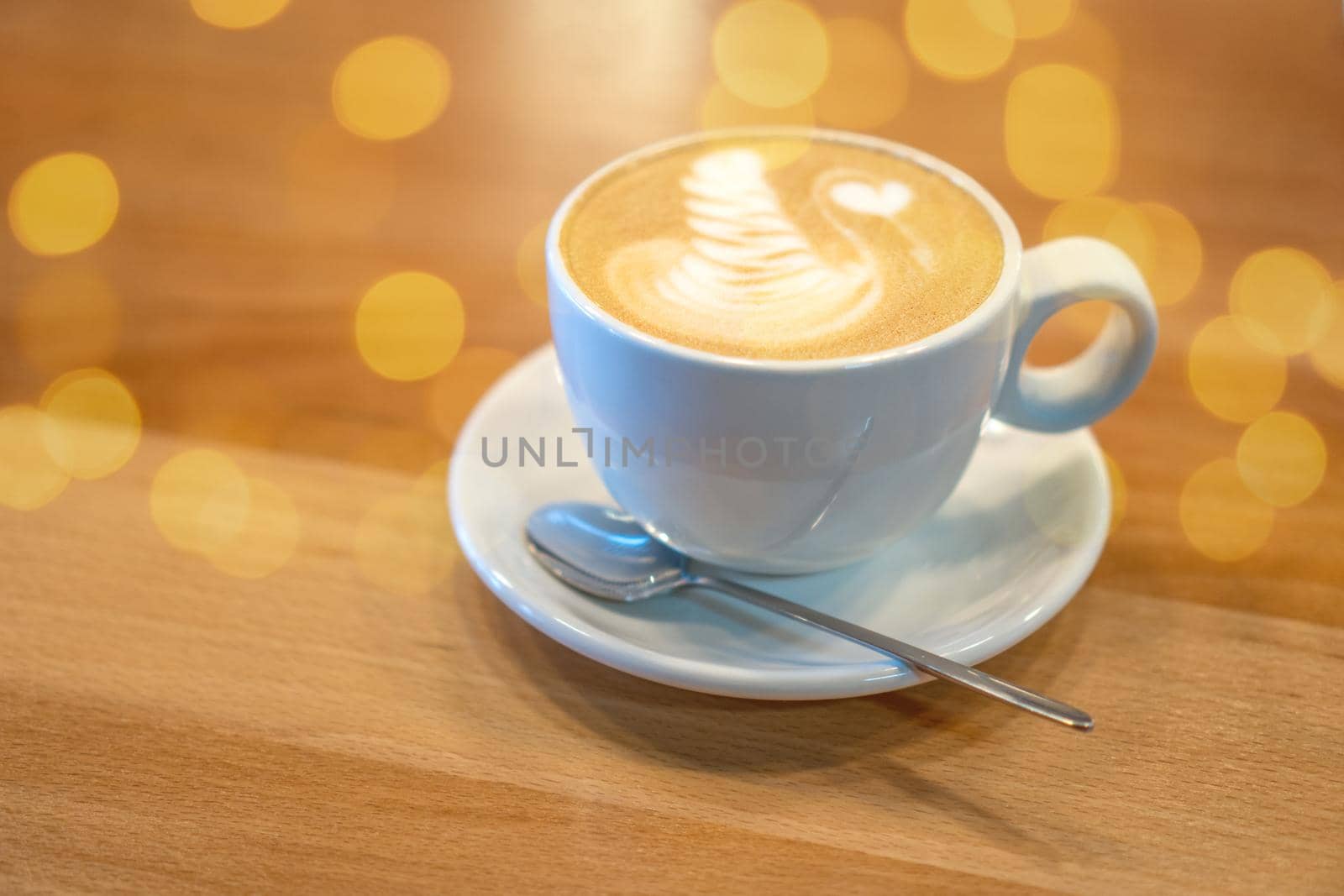 White cup of coffee with latte art standing on wooden table in a cafe. Cappuccino with milk decoration. Morning breakfast. Cozy meal with hot beverage concept