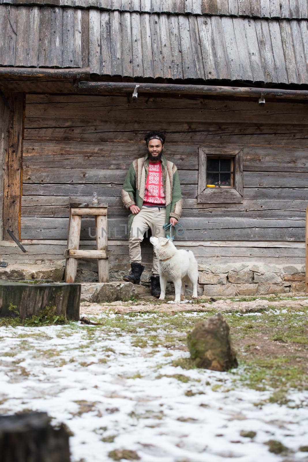 handsome young hipster man standing together with white husky dog in front of old vintage retro wooden house