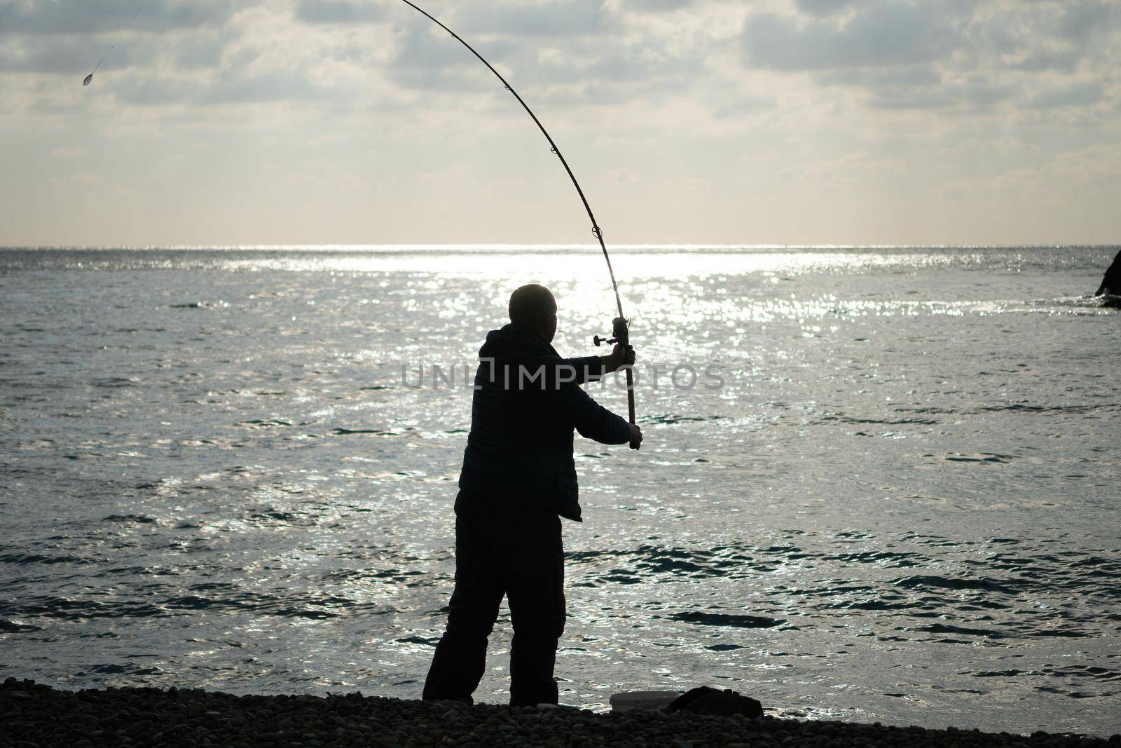 Man hobby fishing on sea tightens a fishing line reel of fish summer. Calm surface sea. Close-up of a fisherman hands twist reel with fishing line on a rod. Fishing in the blue sea outdoors