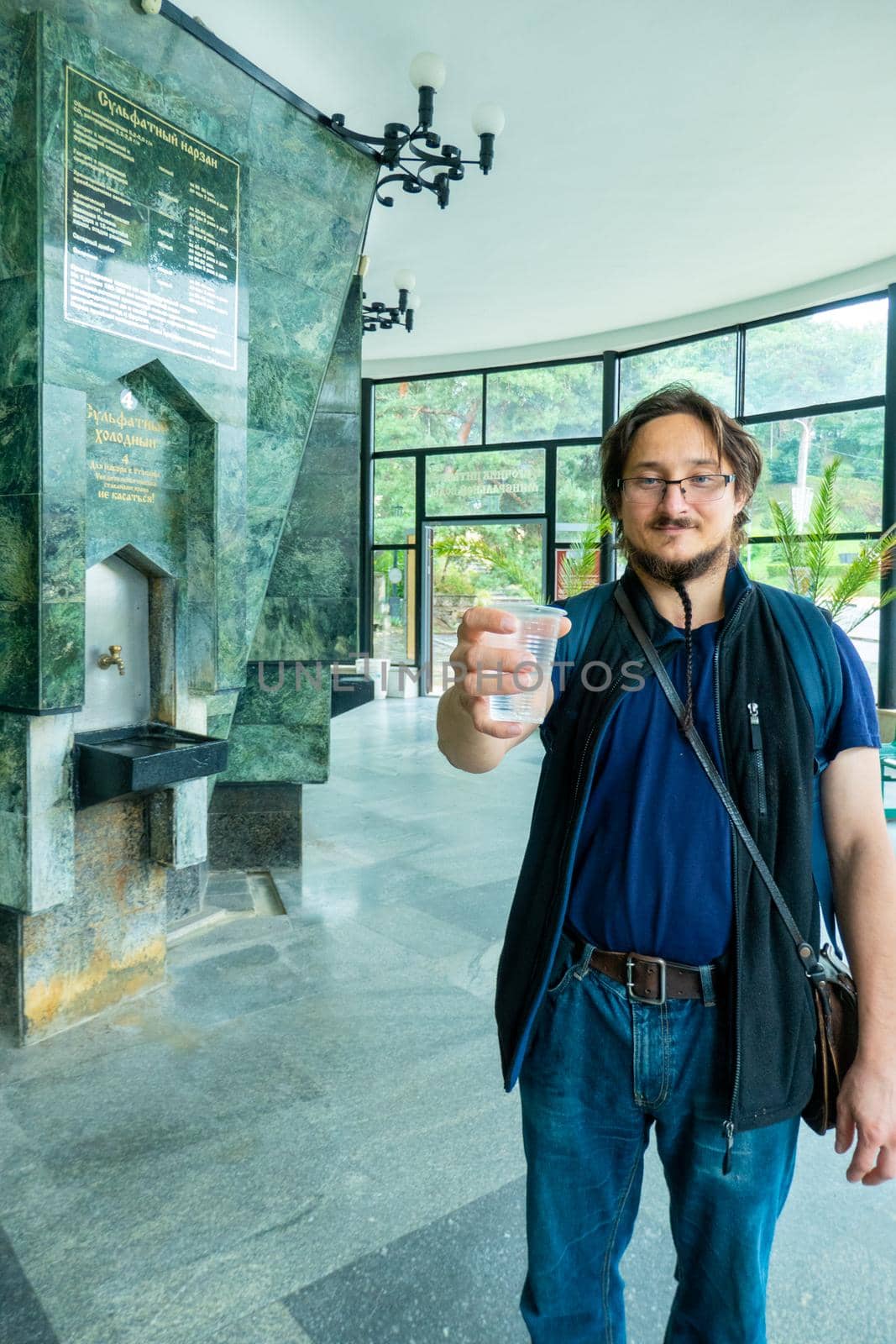 A man gives mineral thermal water in the disposable cup at the pump-room, close-up by kajasja