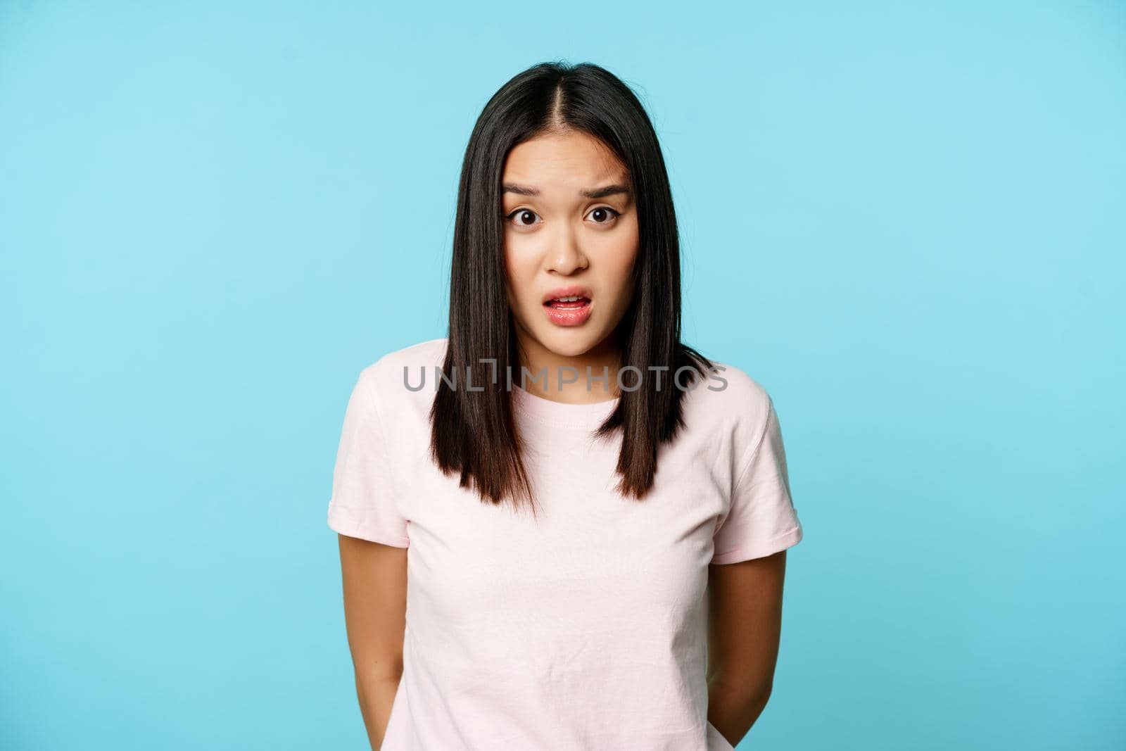 Image of asian korean girl look surprised, raising eyebrows confused, cant understand, standing over blue background by Benzoix