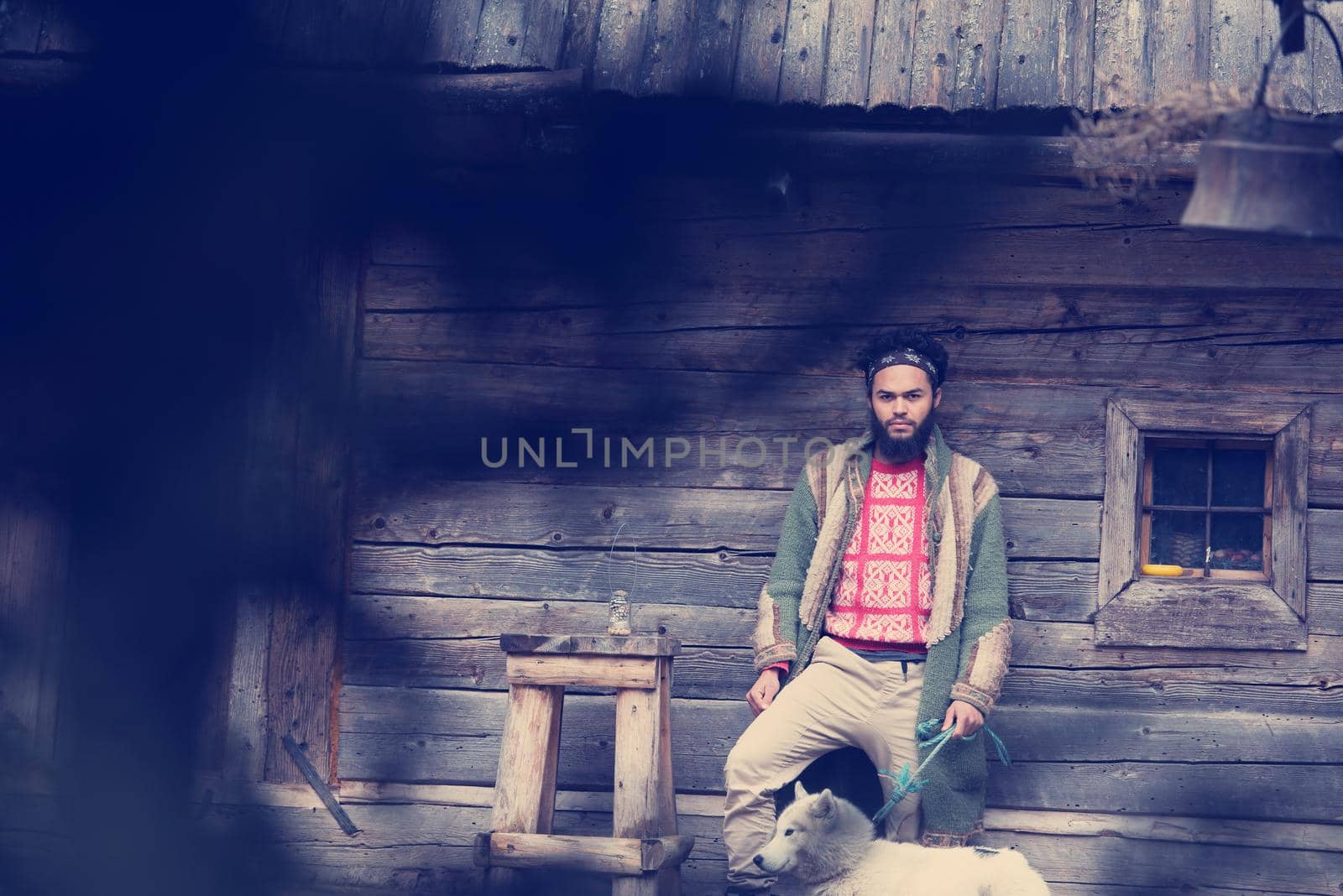 handsome young hipster man standing together with white husky dog in front of old vintage retro wooden house